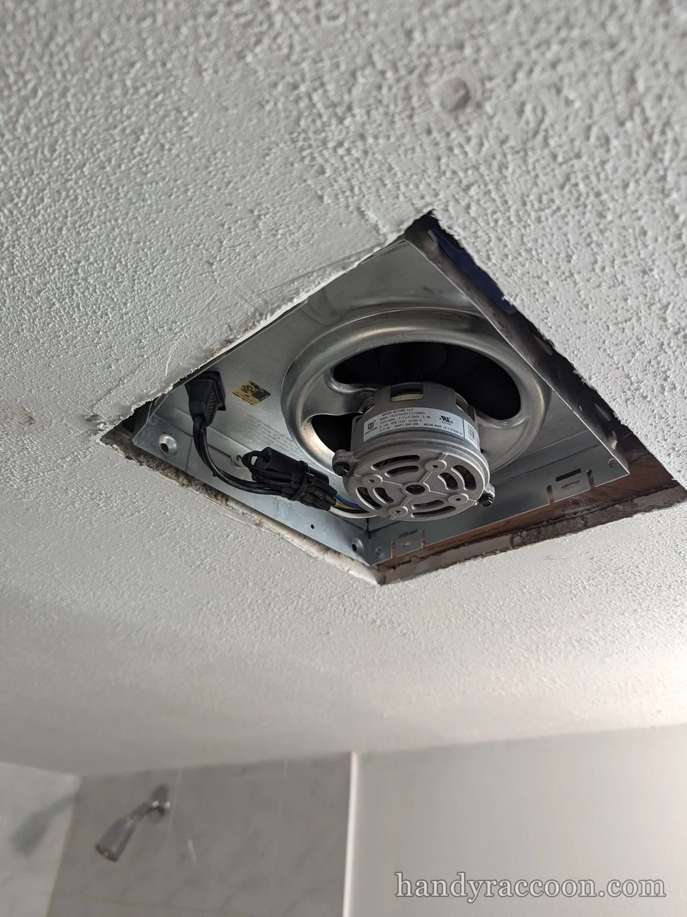 Metal bathroom exhaust fan housing and motor installed in a popcorn ceiling opening.