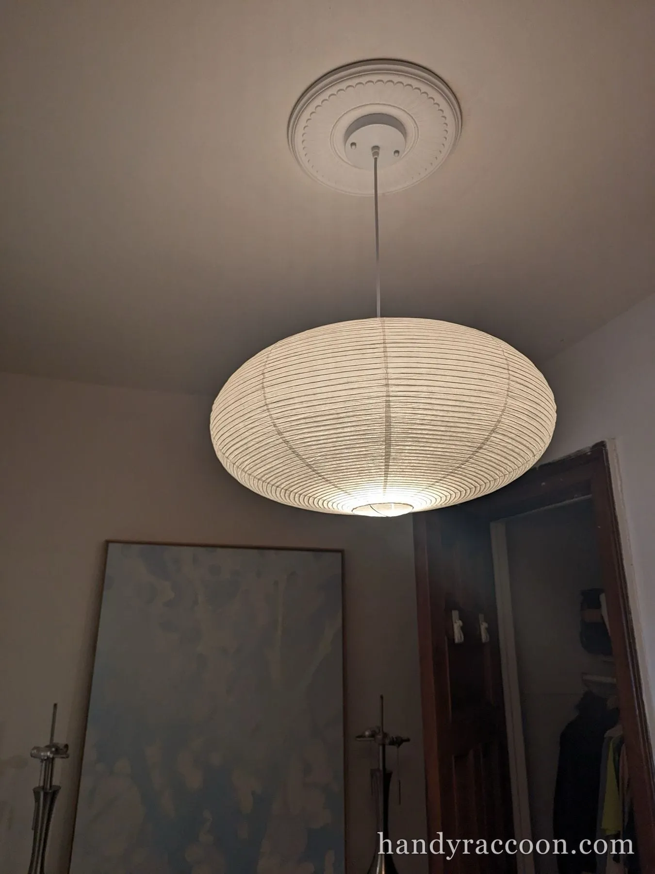 White ribbed paper oval pendant light hanging from a ceiling medallion, lit.