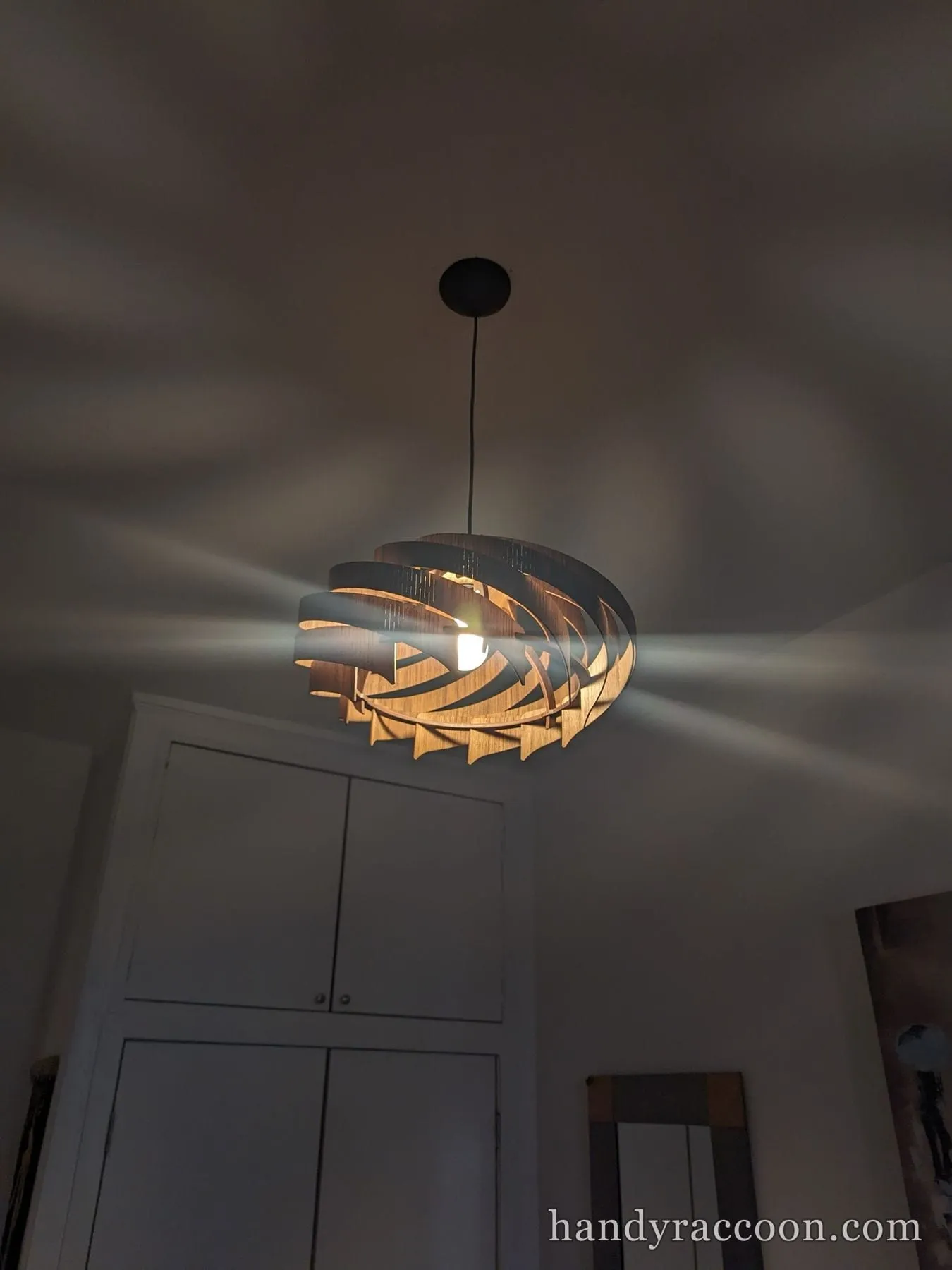 Wooden spiral slatted pendant light glowing and casting patterns on the ceiling.