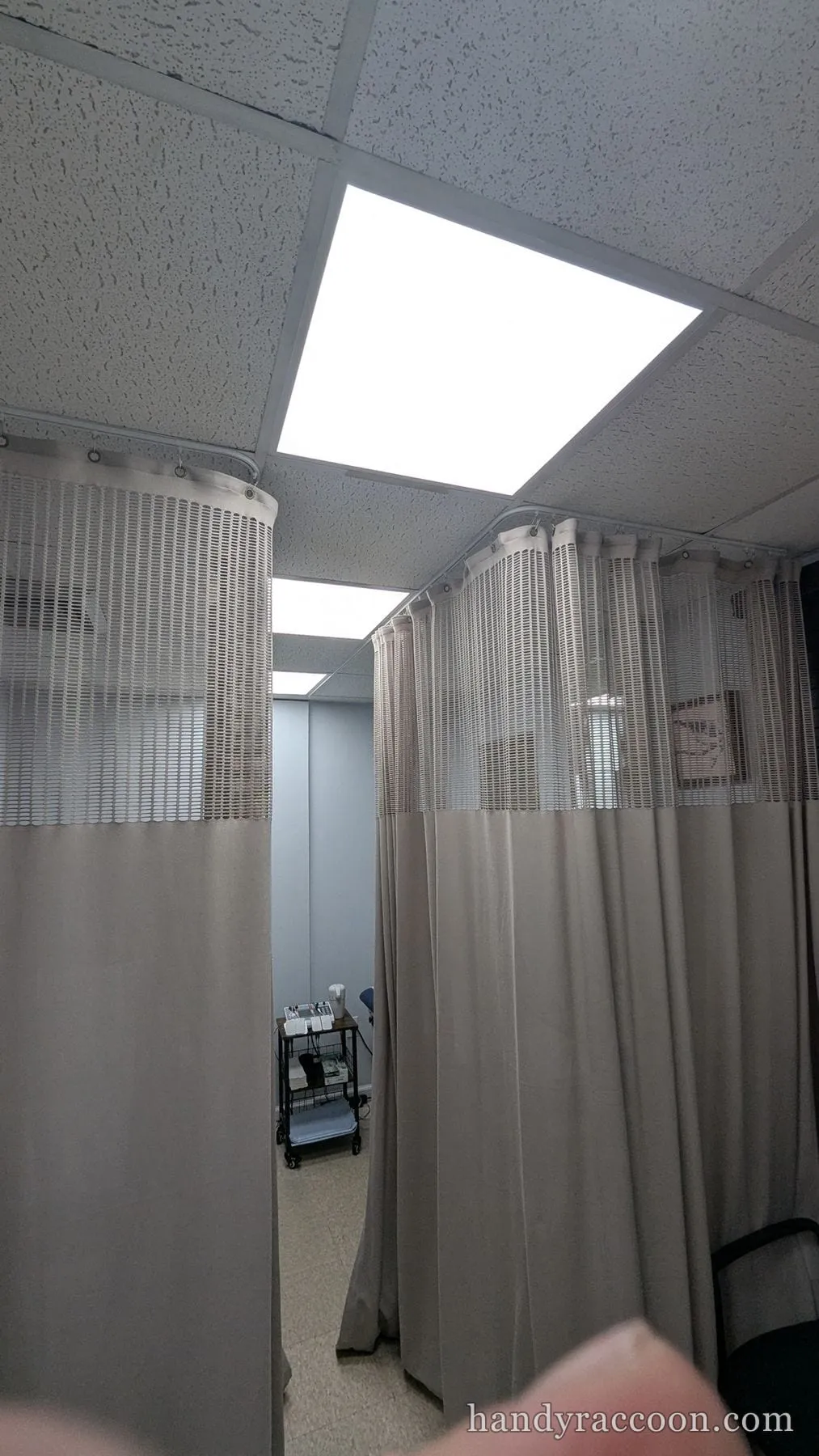 Bright square LED flat panel lit in a drop ceiling above curtained office cubicles.