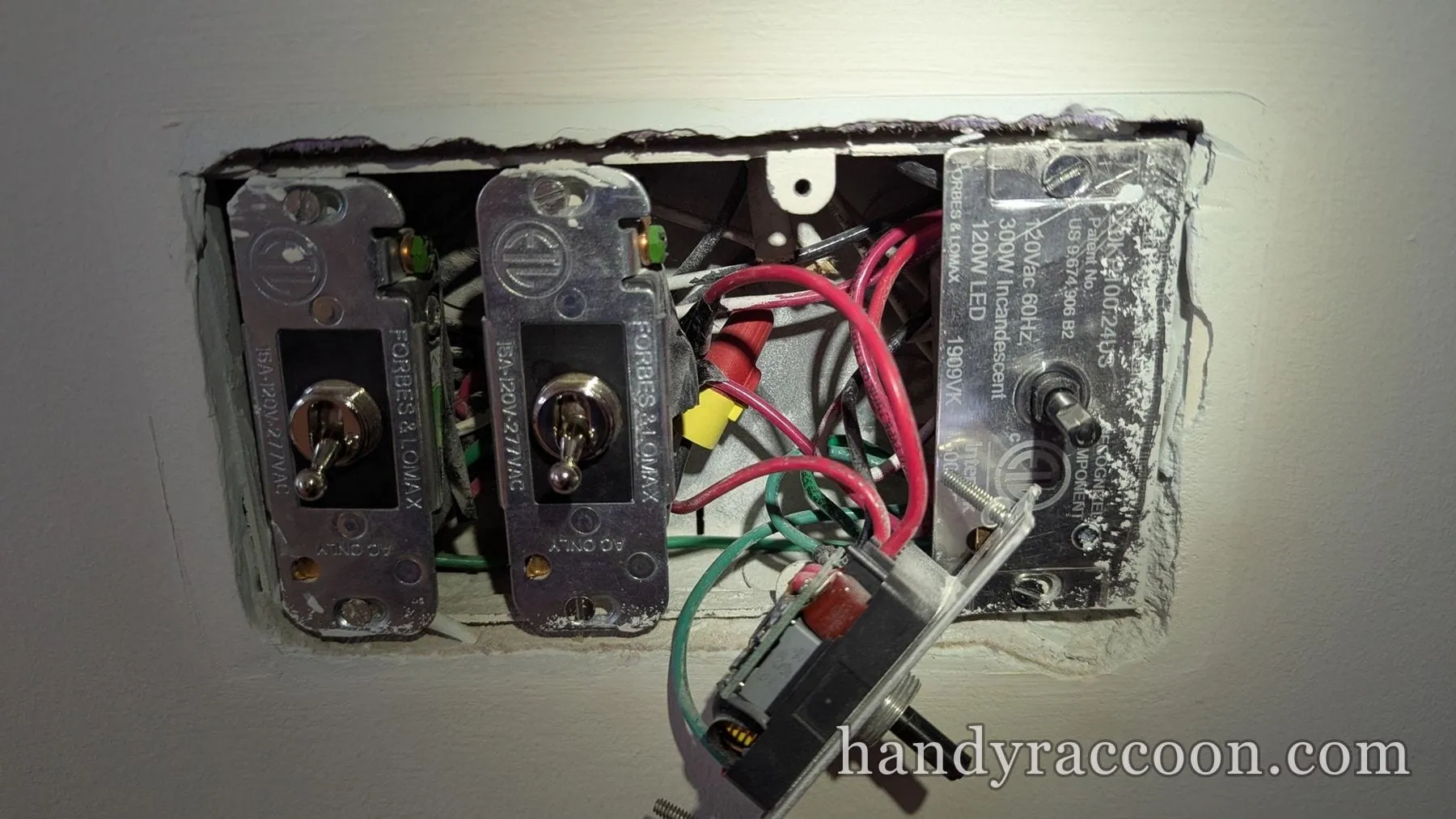 Two metal toggle switches installed and a dimmer module pulled out with wiring exposed.