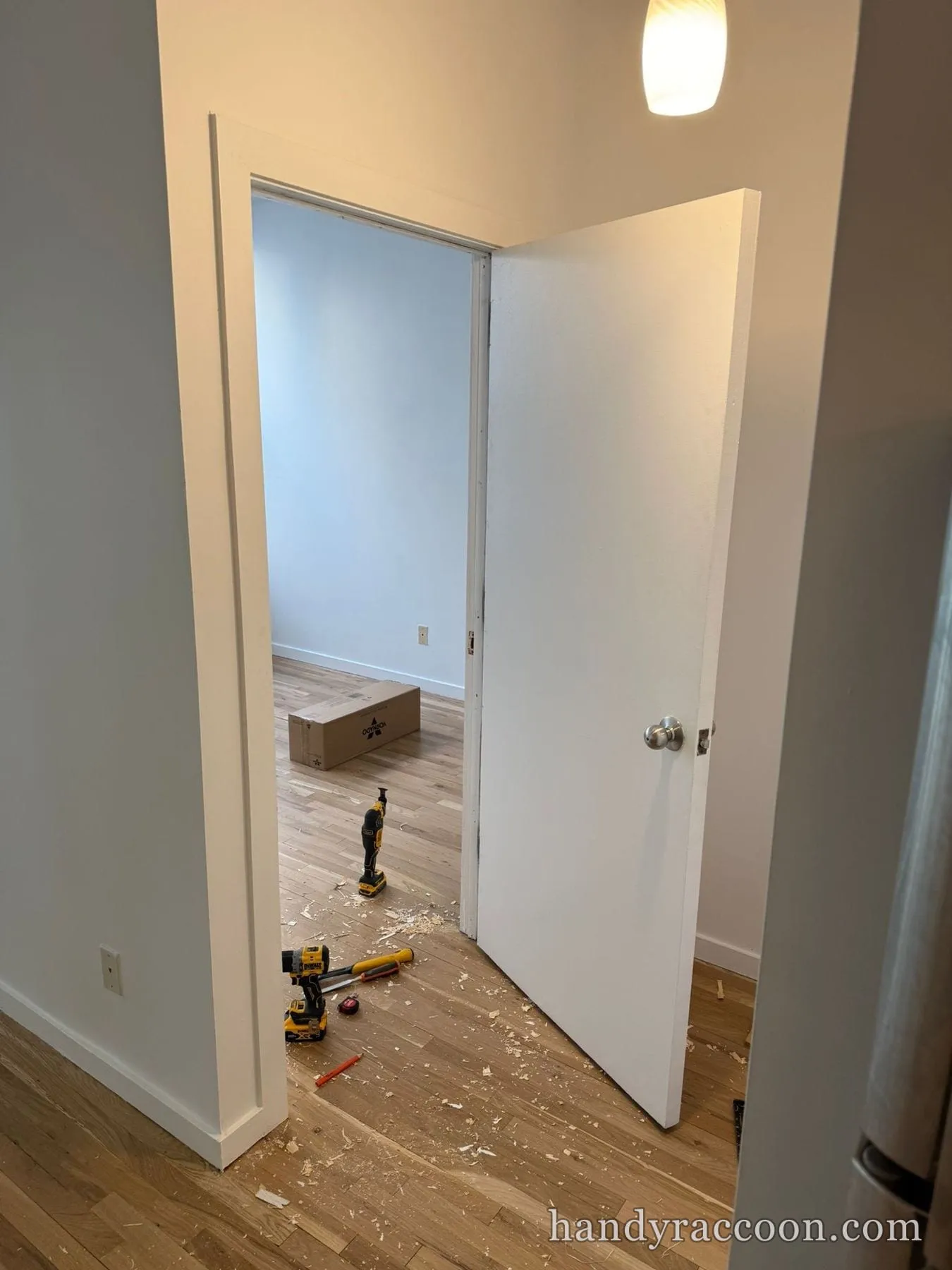 White interior door hung in a doorway with power tools and wood shavings on the floor.