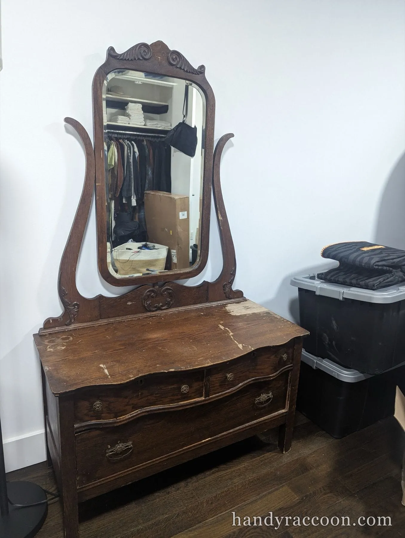 Worn antique wooden dresser with a tall swing mirror in a bedroom corner.