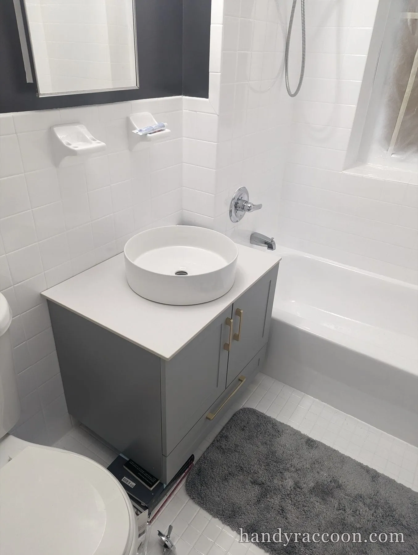Gray bathroom vanity cabinet with a white round vessel sink next to a white tub.