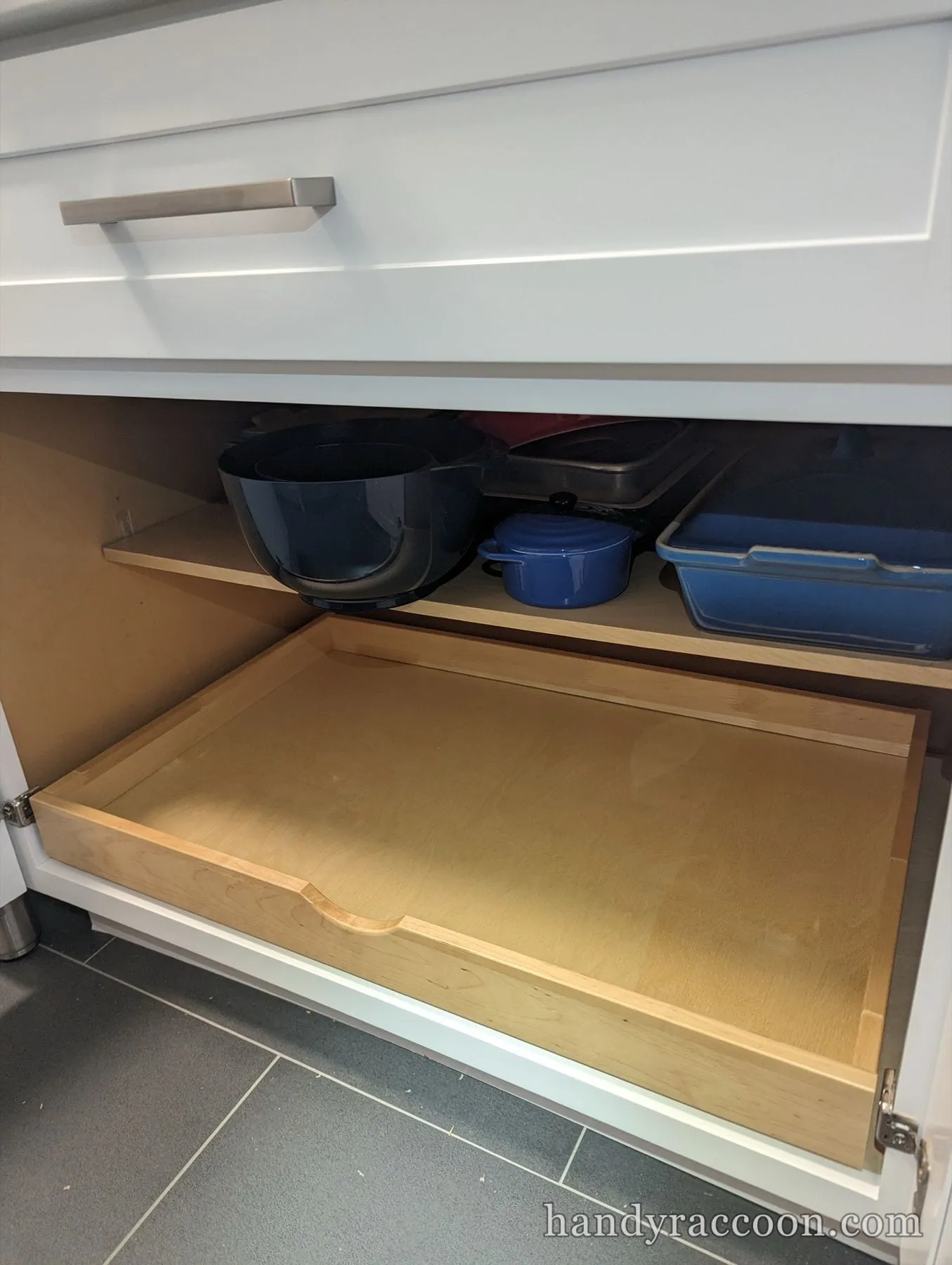 Maple roll out shelf installed in a white lower kitchen cabinet holding cookware.
