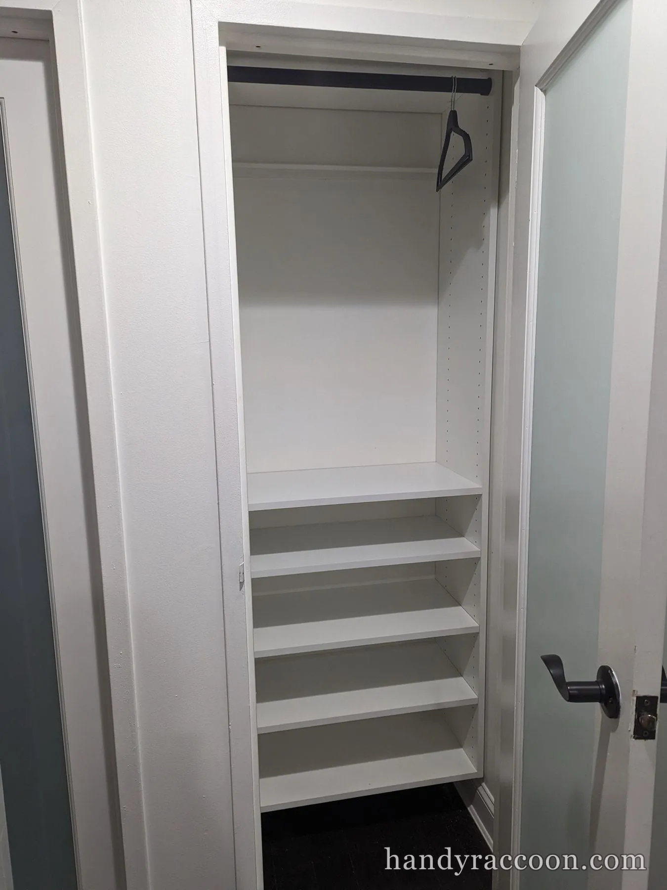Narrow closet with five white shelves and a hanging rod holding one hanger.
