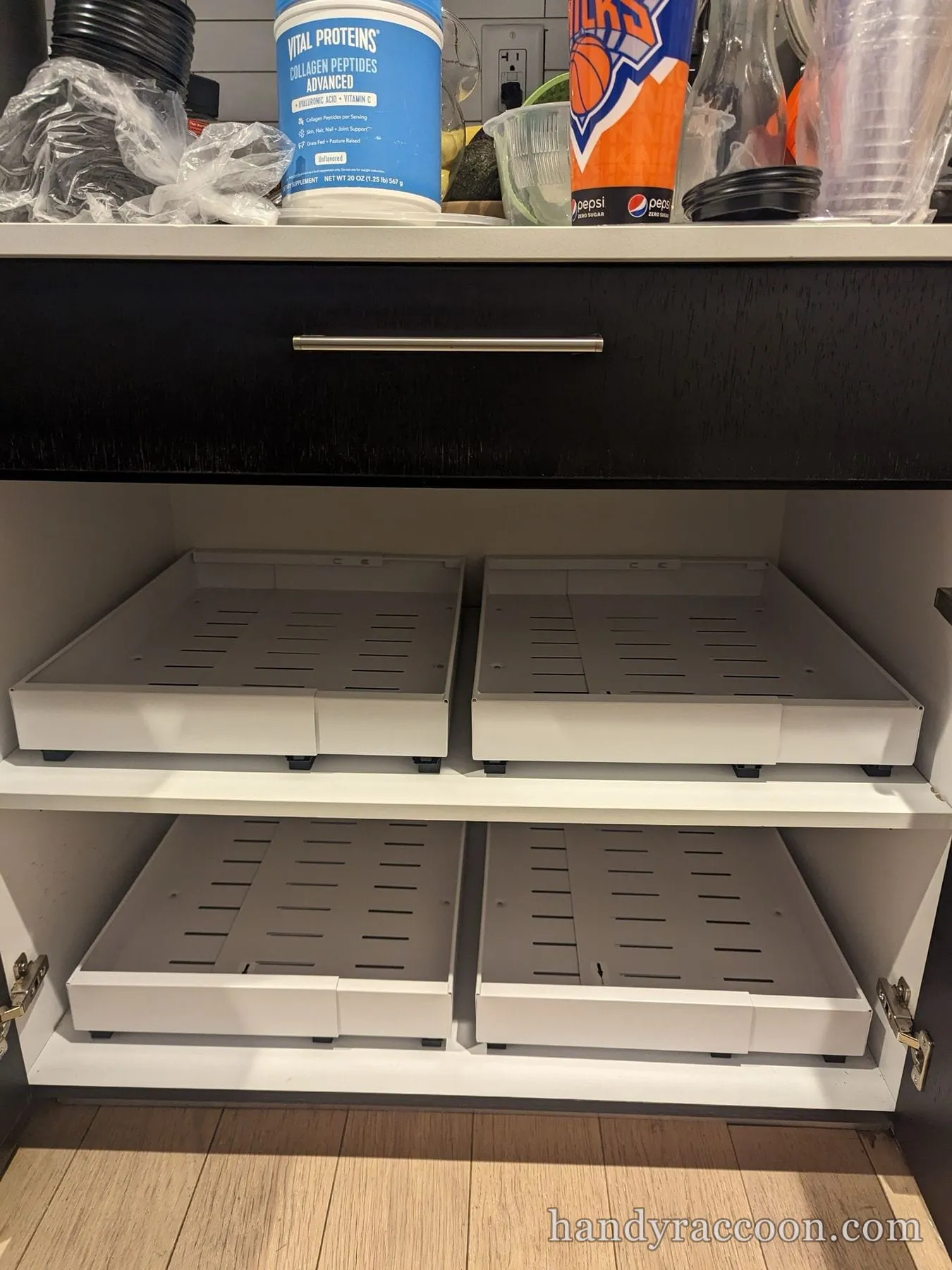 Four gray pull out sliding trays on two levels inside a dark base kitchen cabinet.