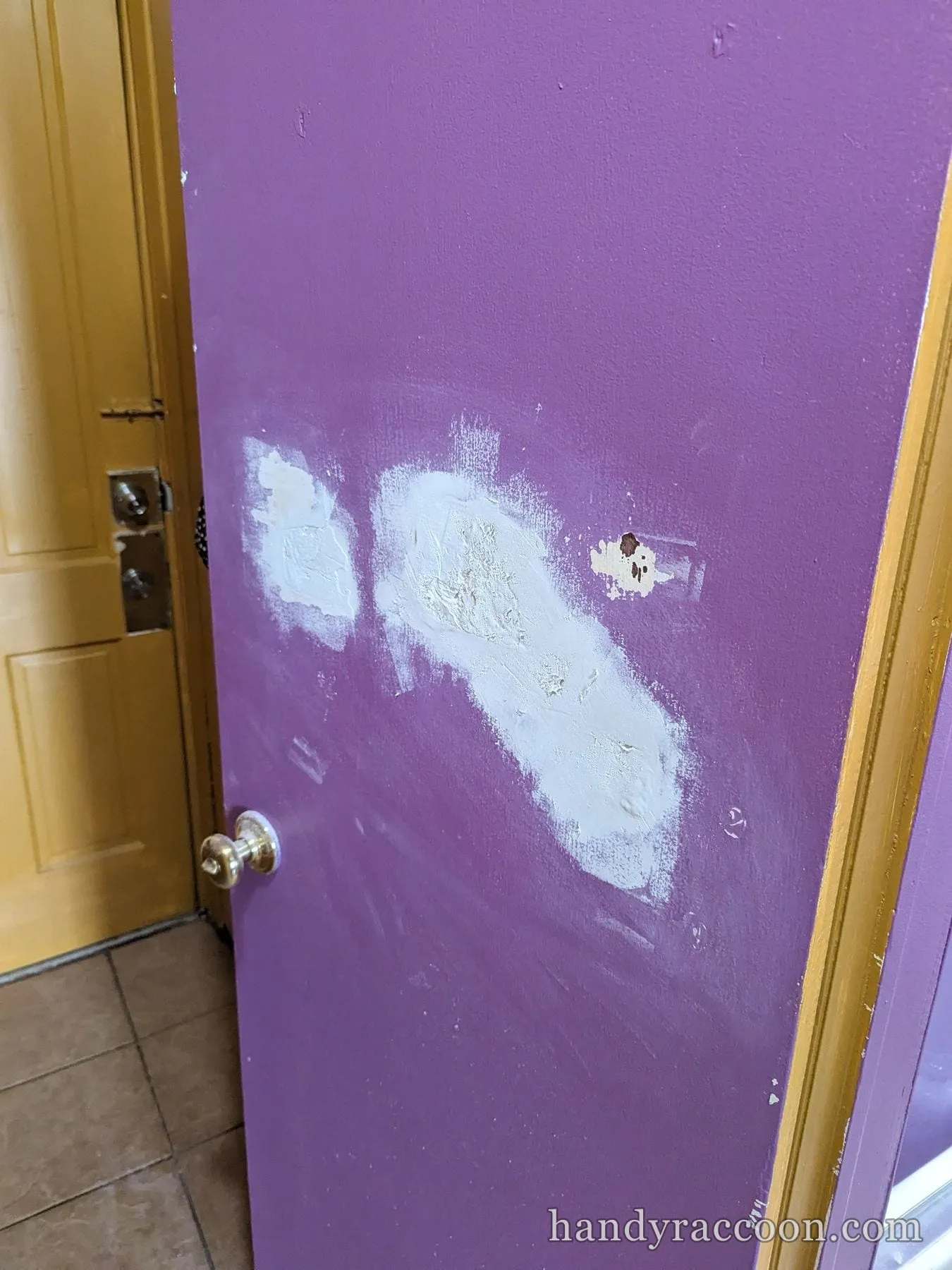 Purple door with white spackle patches over former hardware holes near the knob.