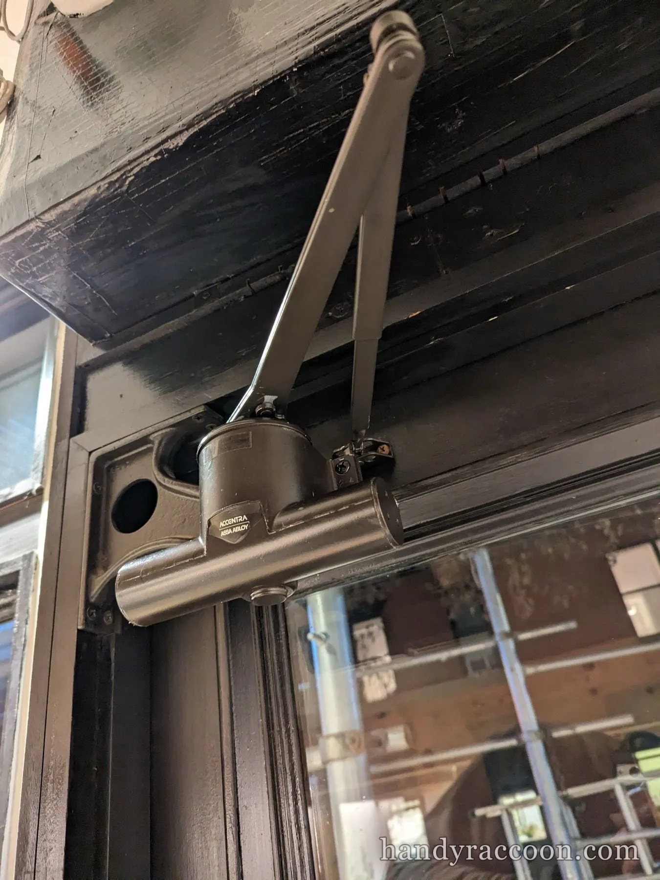 Bronze hydraulic door closer with its arm mounted at the top of a glass door.