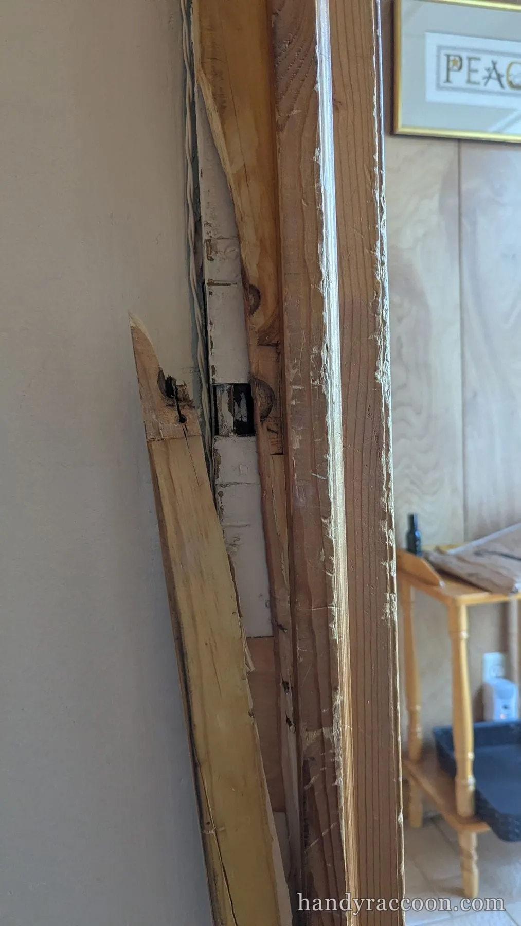 Cracked and splintered wood door jamb with an exposed strike area beside a mirror.