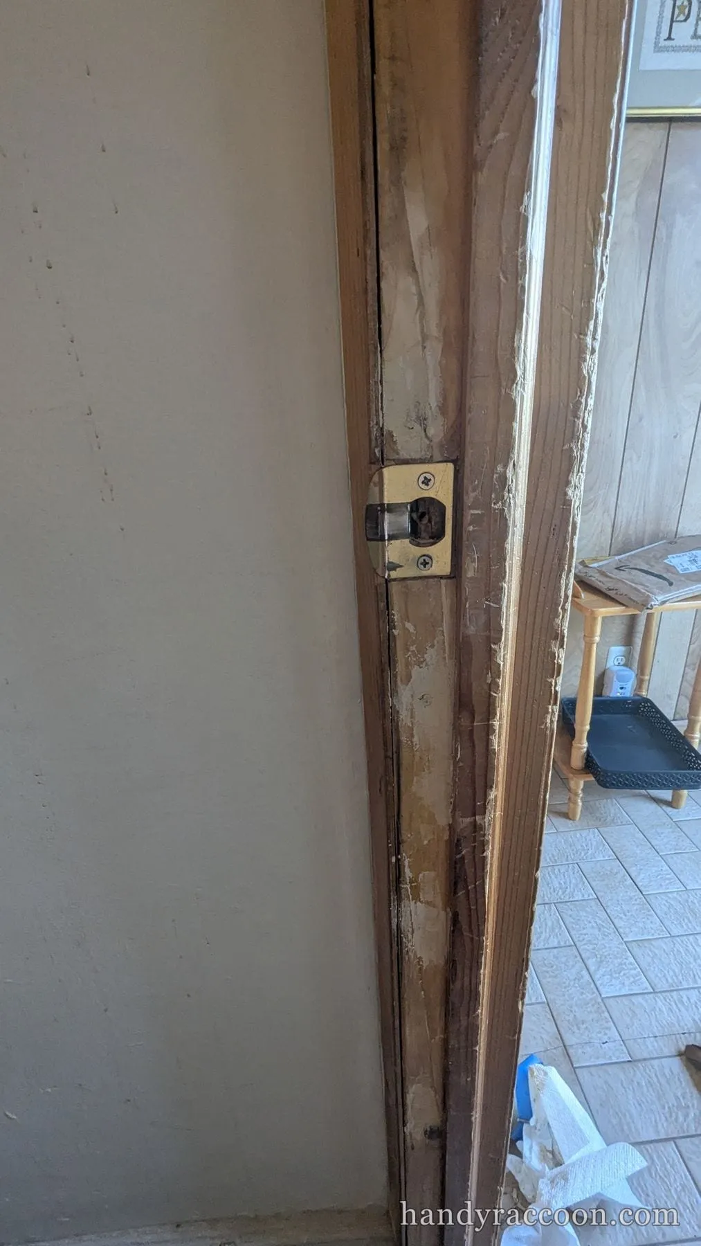 Close-up of a brass strike plate on a wood door jamb with light wood filler patched around it.
