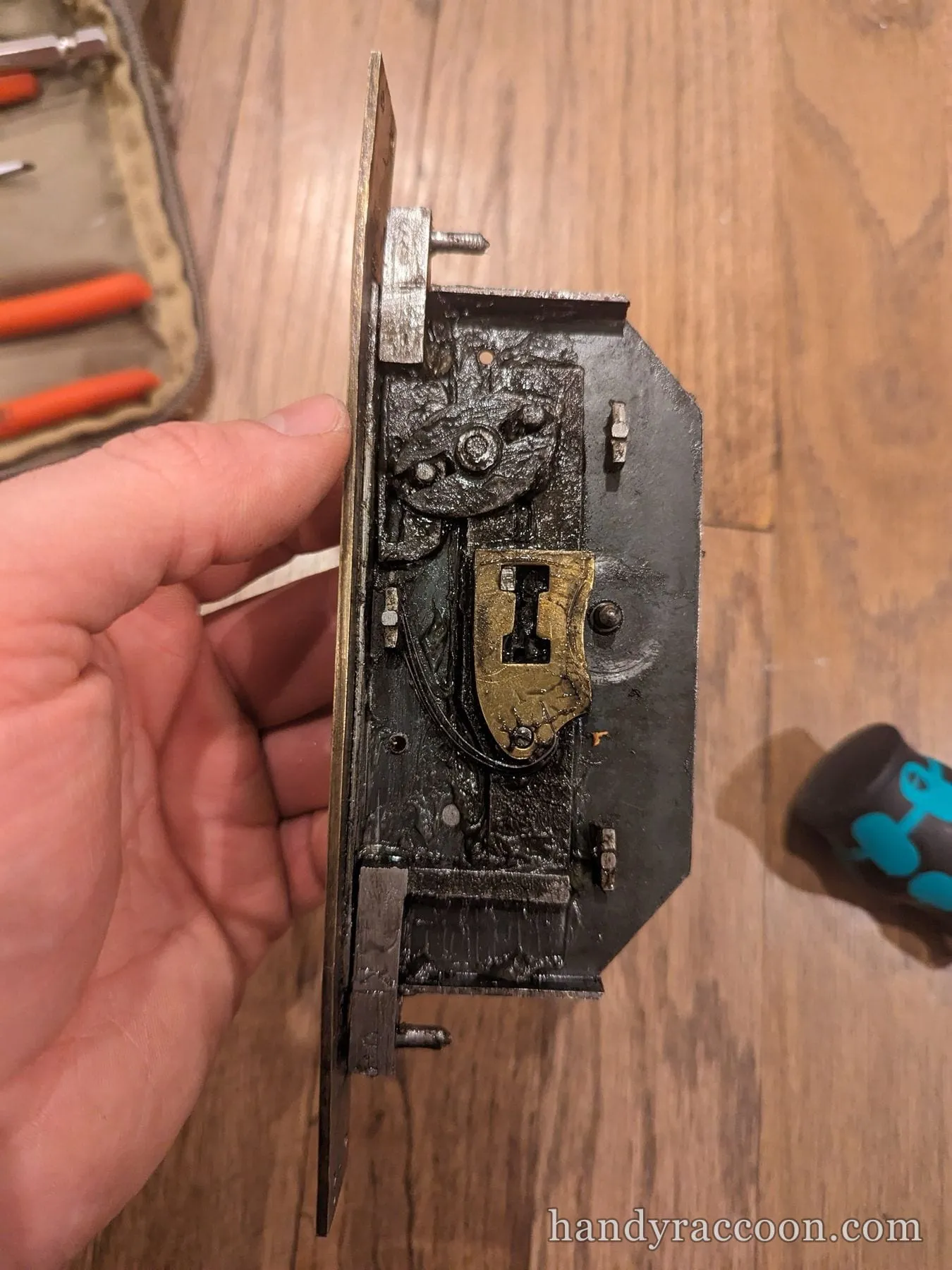 Hand holding an opened antique mortise lock showing its brass and steel internal parts.