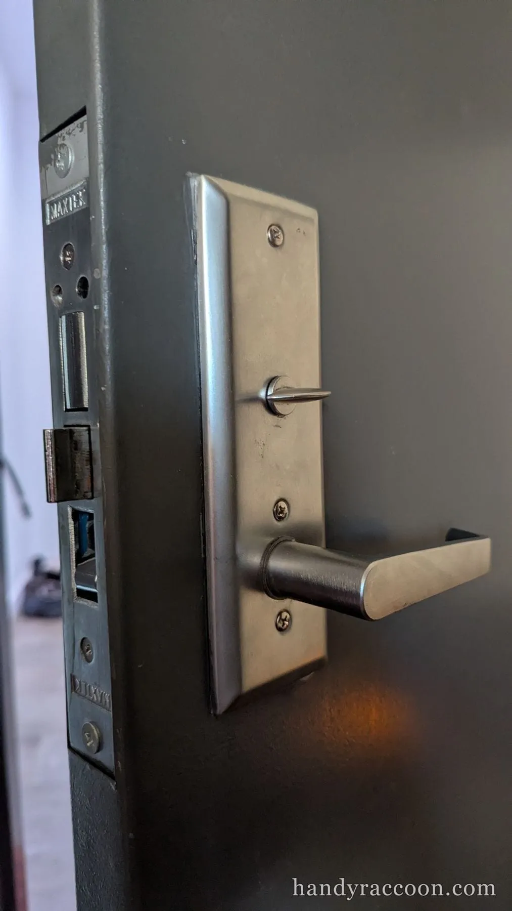 Gray door with a brushed stainless mortise lockset, lever handle, and turn-piece installed.