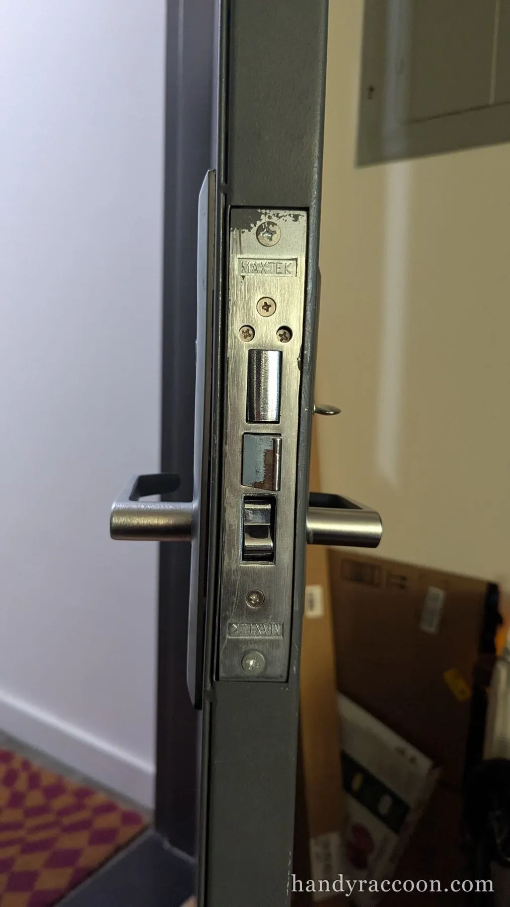 Edge of a gray door showing a stainless mortise lock faceplate with deadbolt and latch.