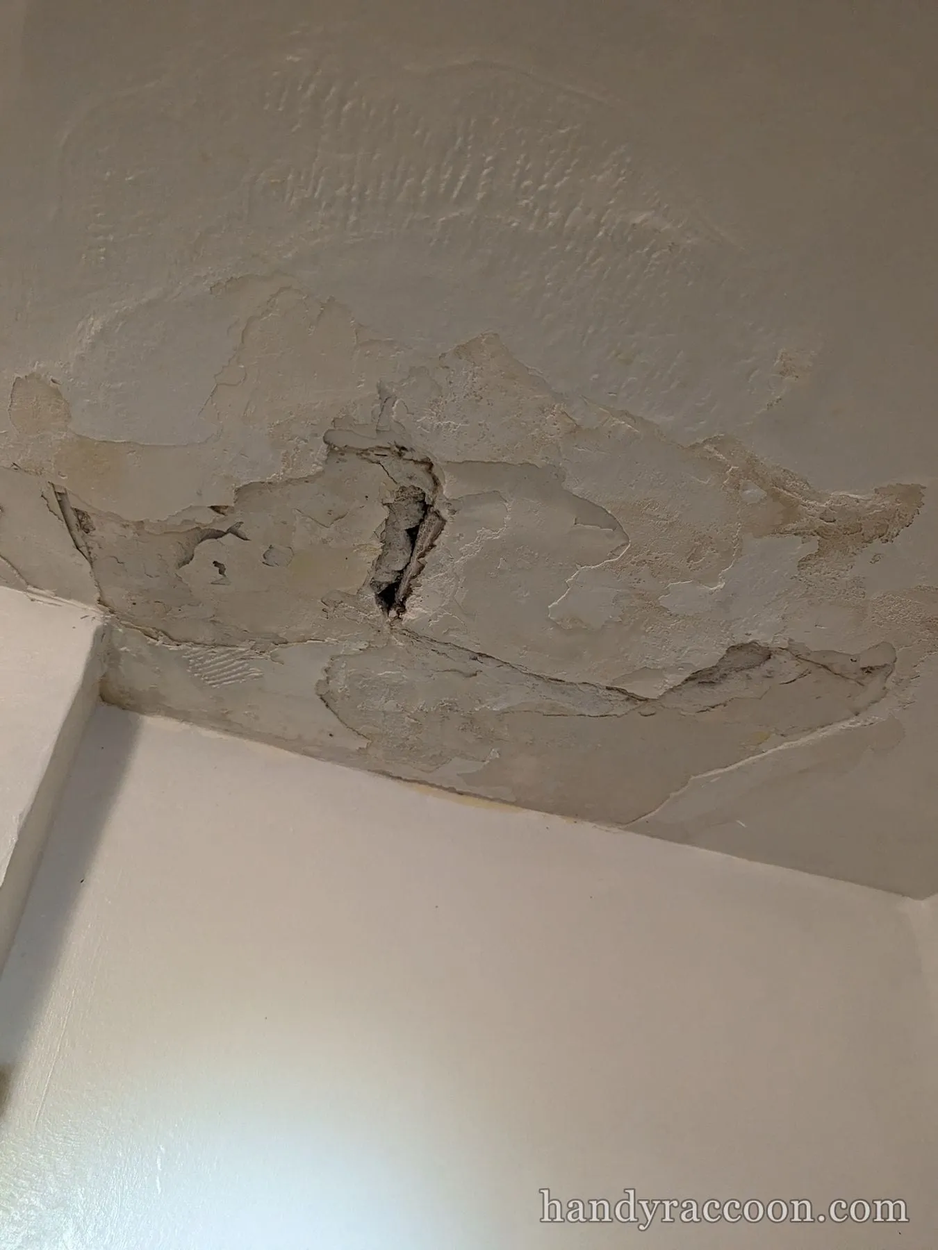 Close-up of a ceiling corner with peeling and cracked plaster showing water damage.