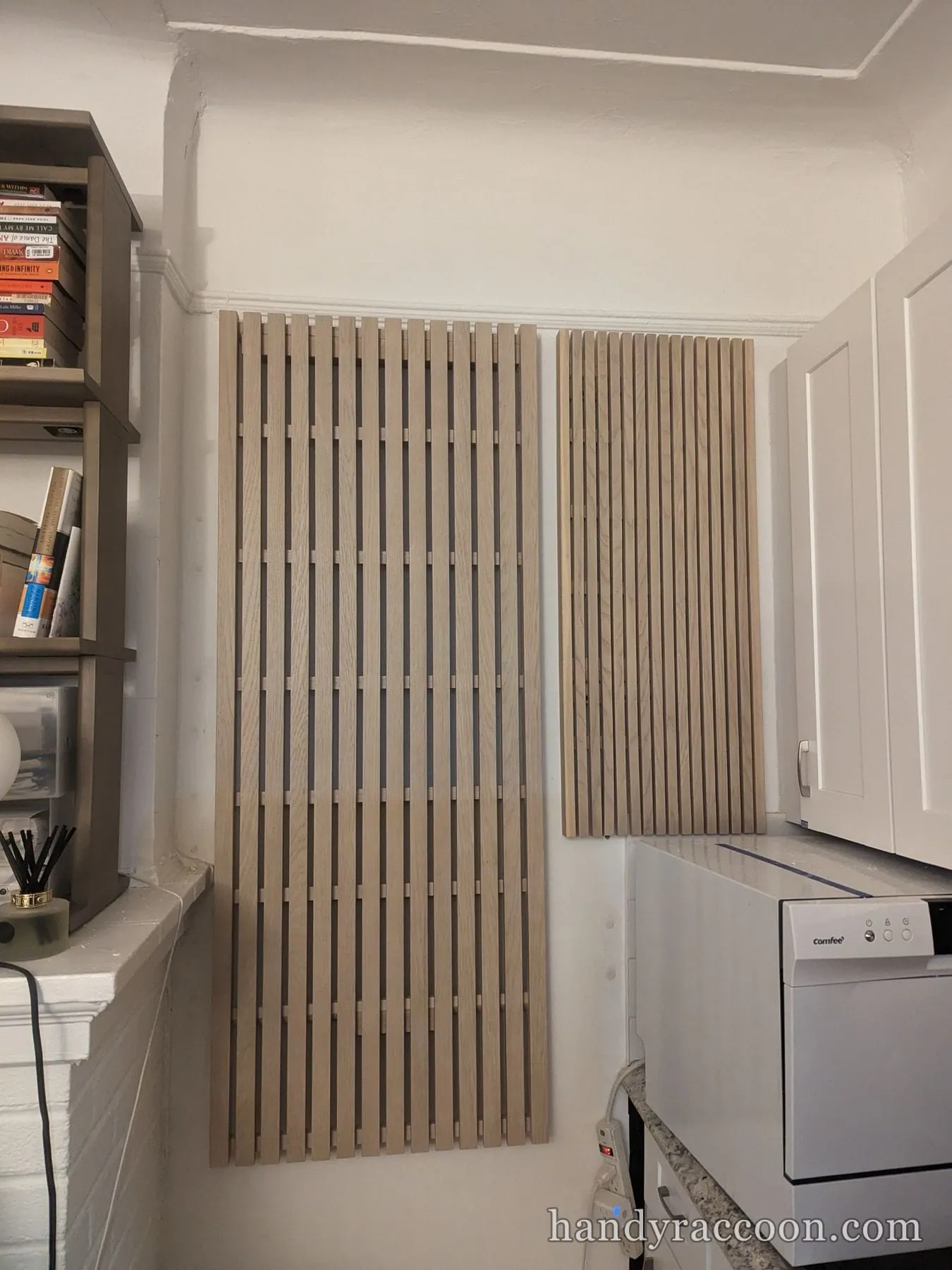 Two vertical wood slat wall panels mounted on a white wall next to a bookshelf and a dishwasher.