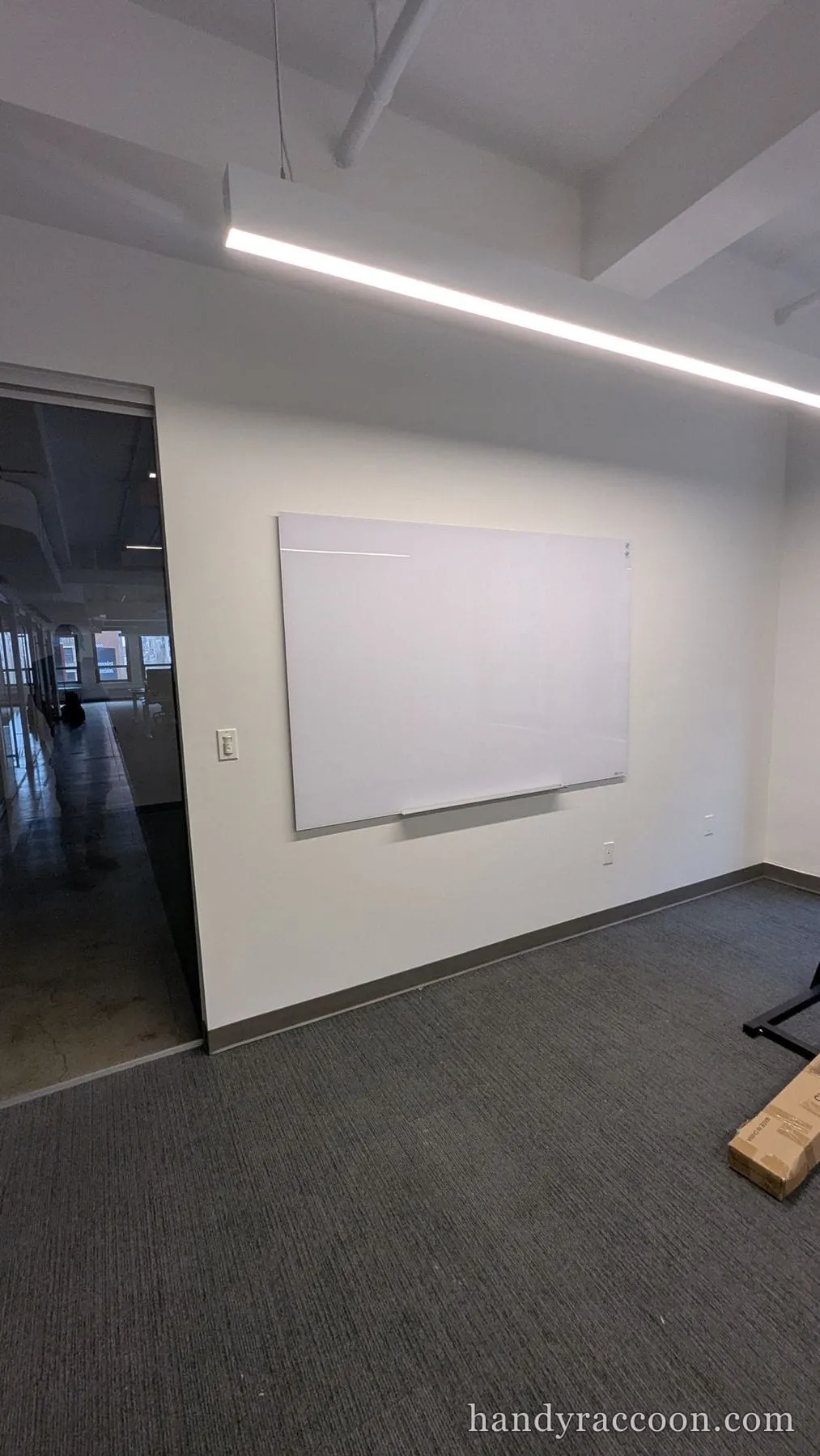 A frosted glass dry-erase board mounted on a wall in a carpeted office beside a glass partition.