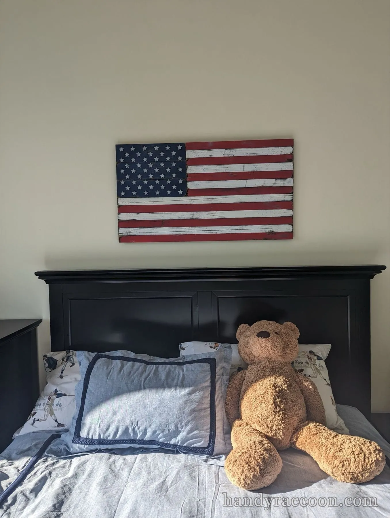 Distressed wood American flag artwork mounted on the wall above a black headboard and bed.