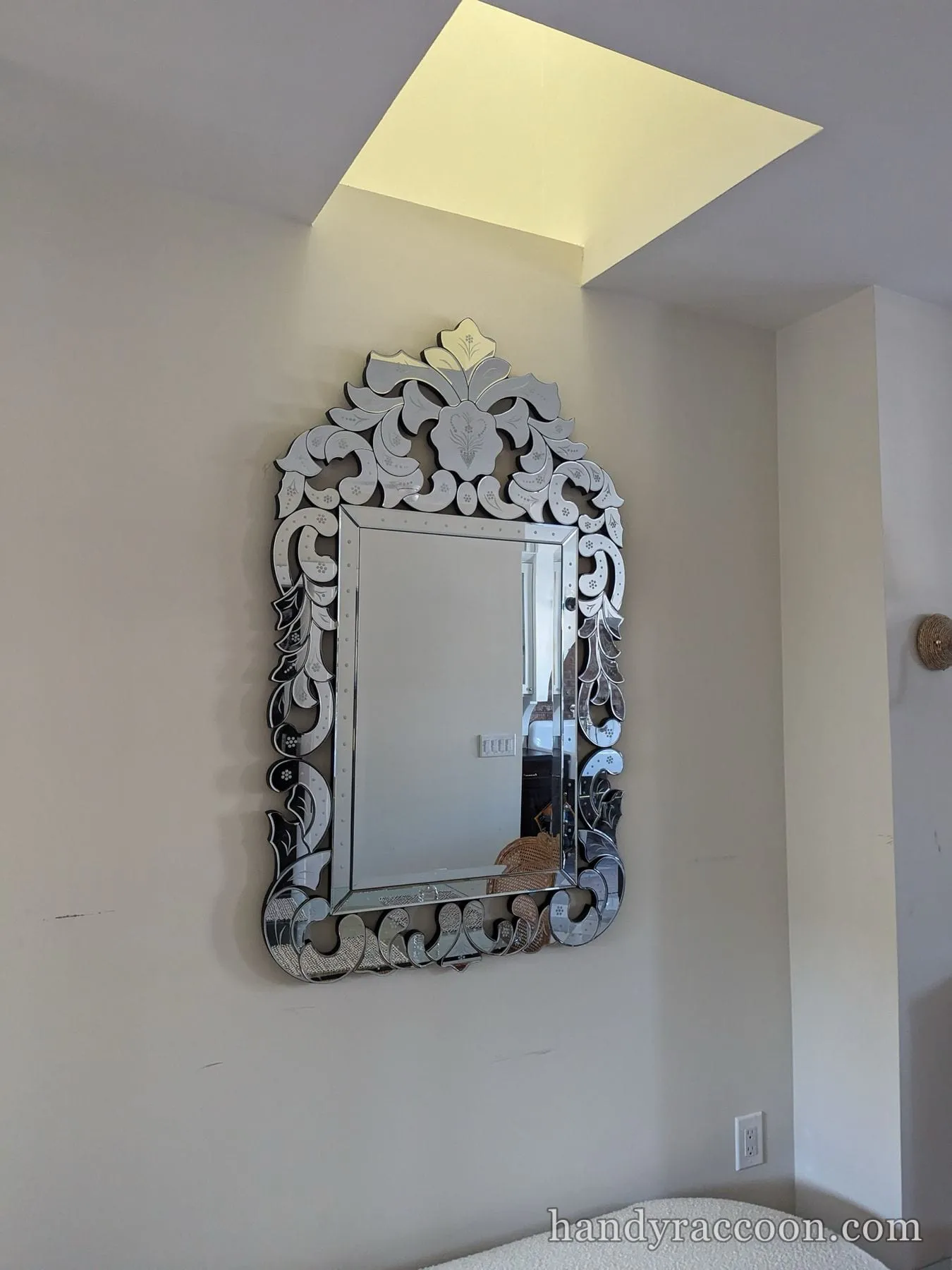 Decorative etched Venetian-style glass mirror hung on a gray bedroom wall.