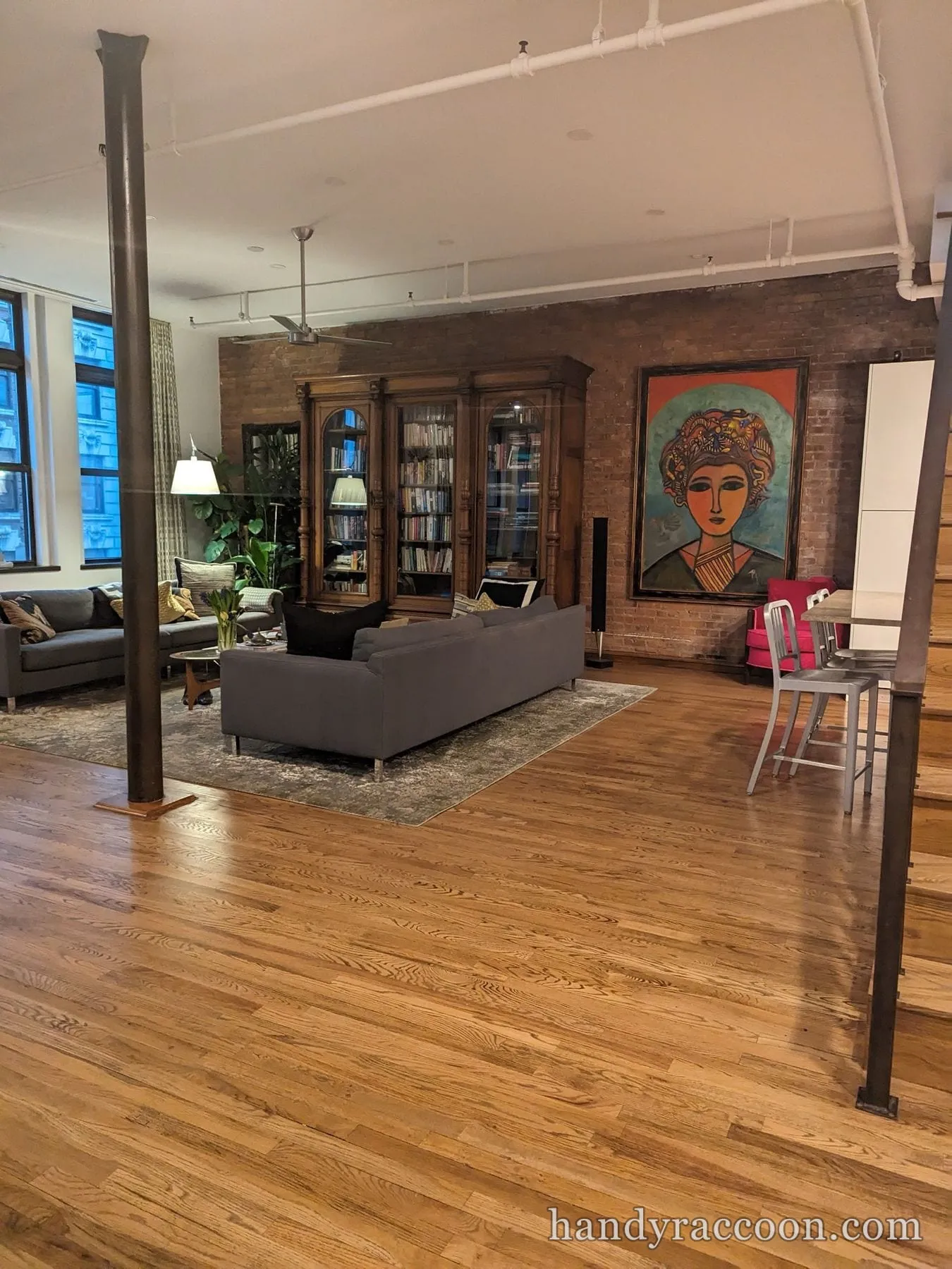 Large framed portrait painting hung on an exposed brick wall in an open loft living room.
