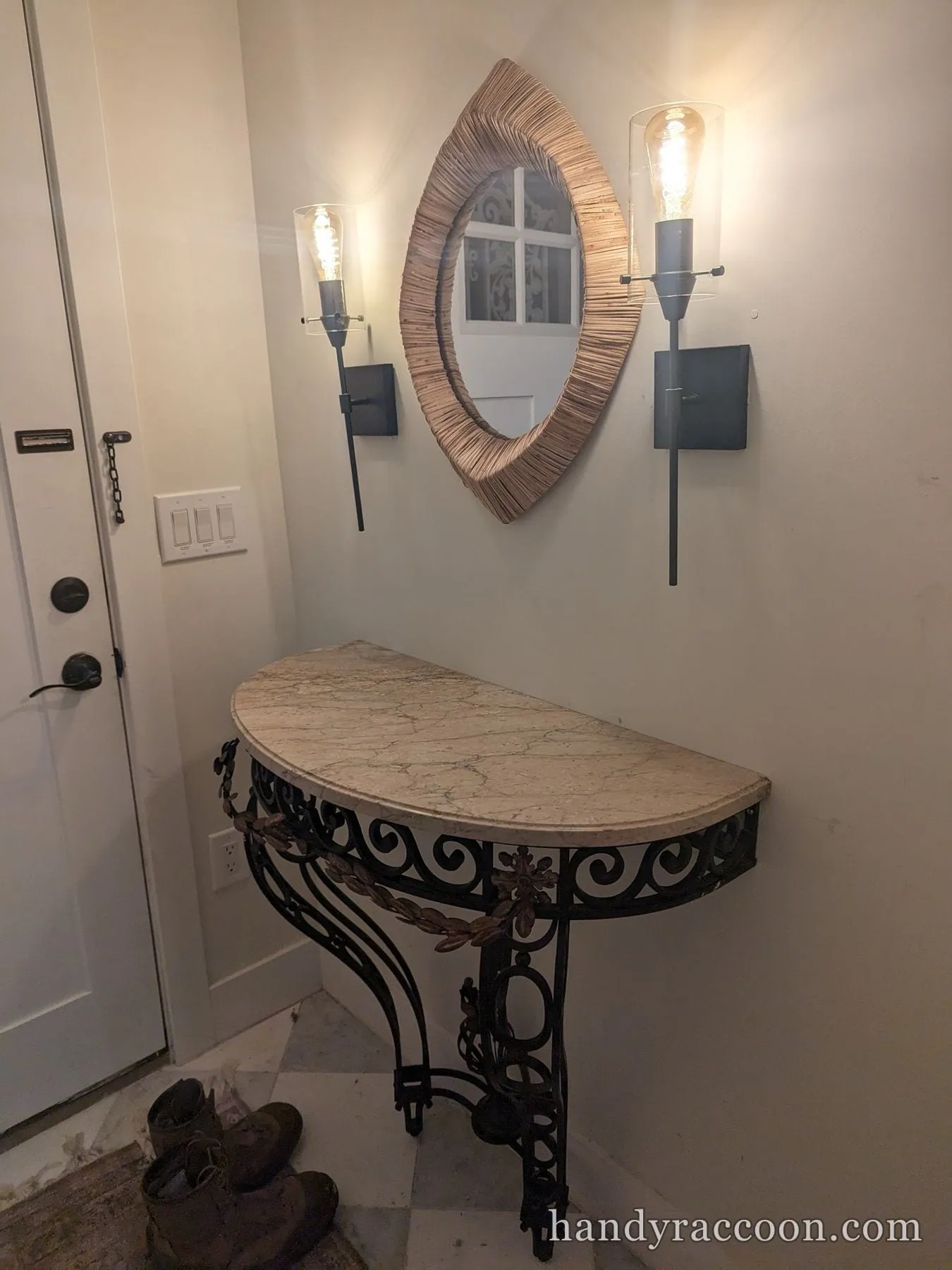 Woven eye-shaped mirror mounted between two lit wall sconces above a marble console table.