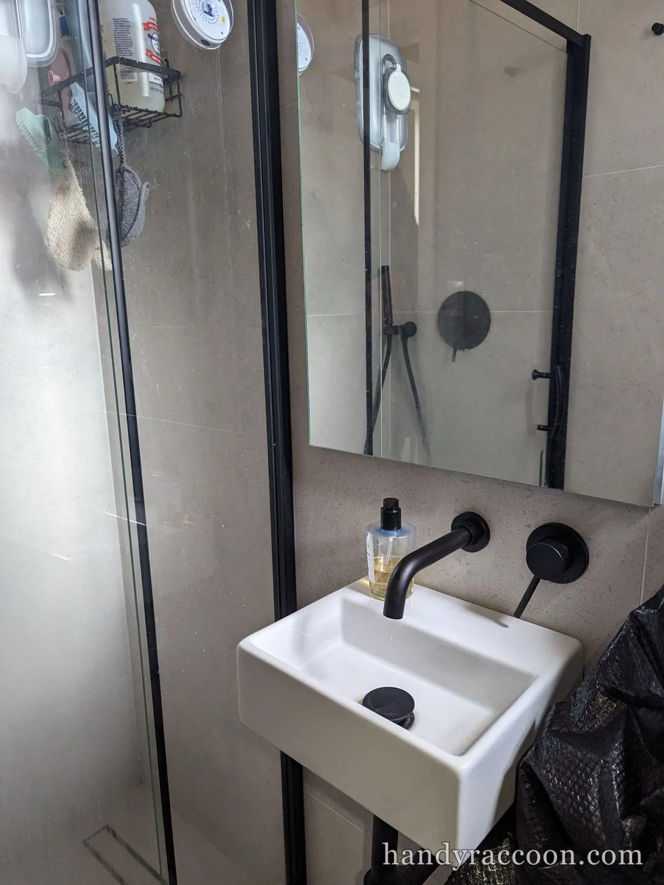 Black-framed mirror mounted on tile above a white wall-hung sink with a black faucet.