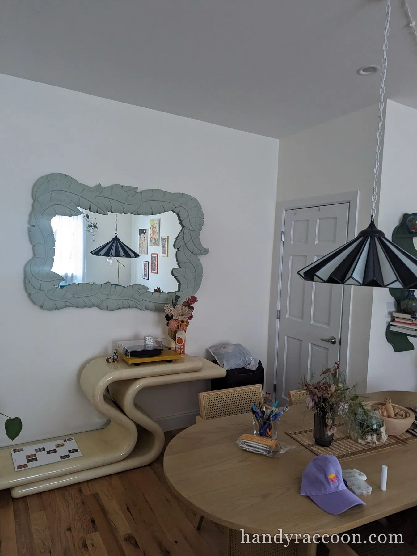 Large sage carved leaf-frame mirror mounted on a wall above a cream curved console.