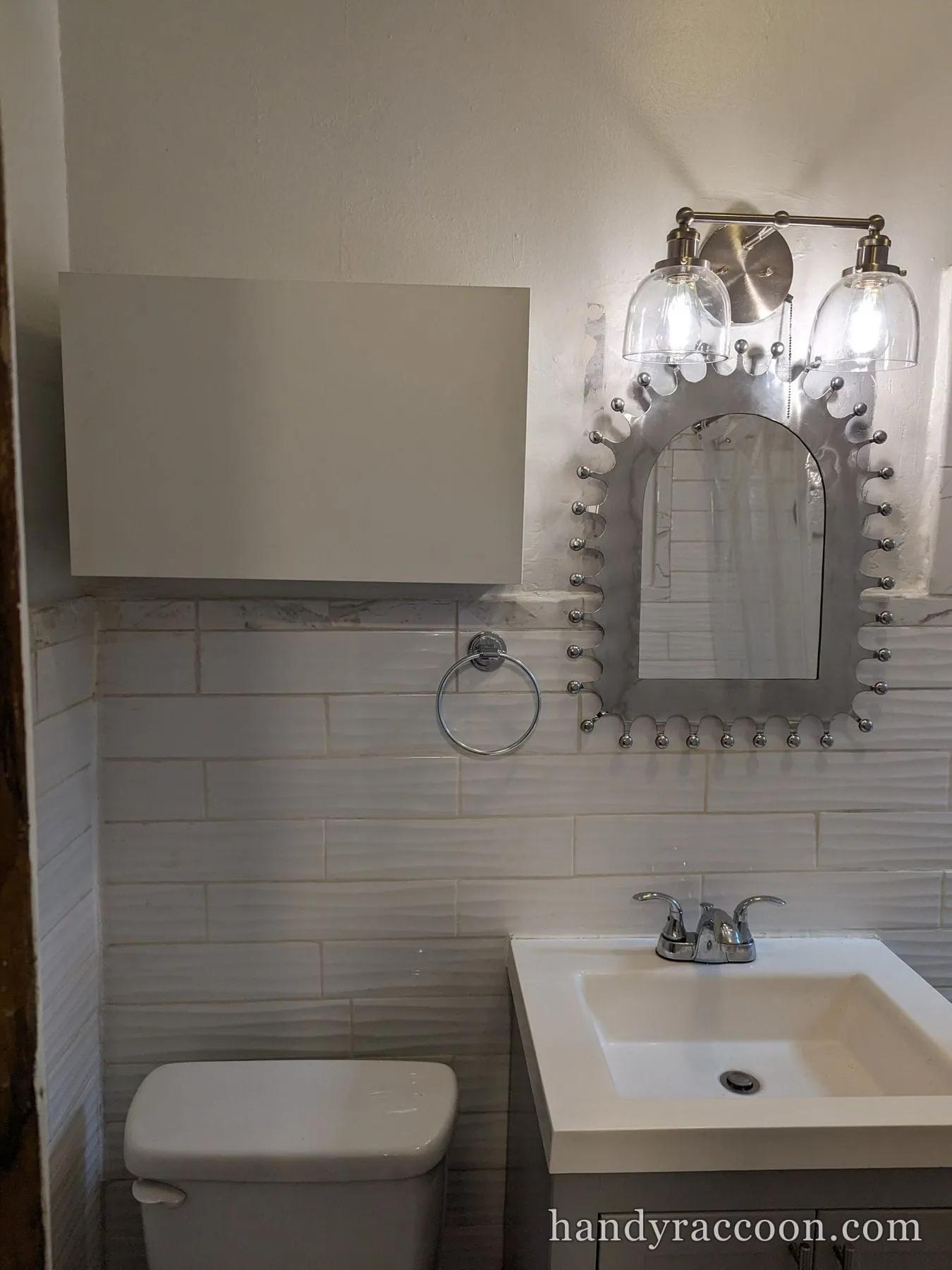 Silver arched mirror and glass-shade vanity light mounted above a bathroom vanity sink.