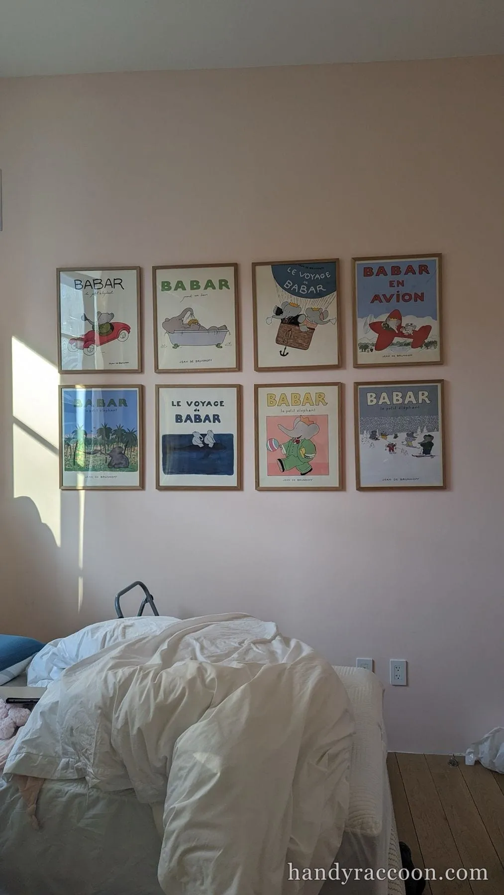 Grid of eight framed vintage Babar posters mounted on a bedroom wall above a bed.
