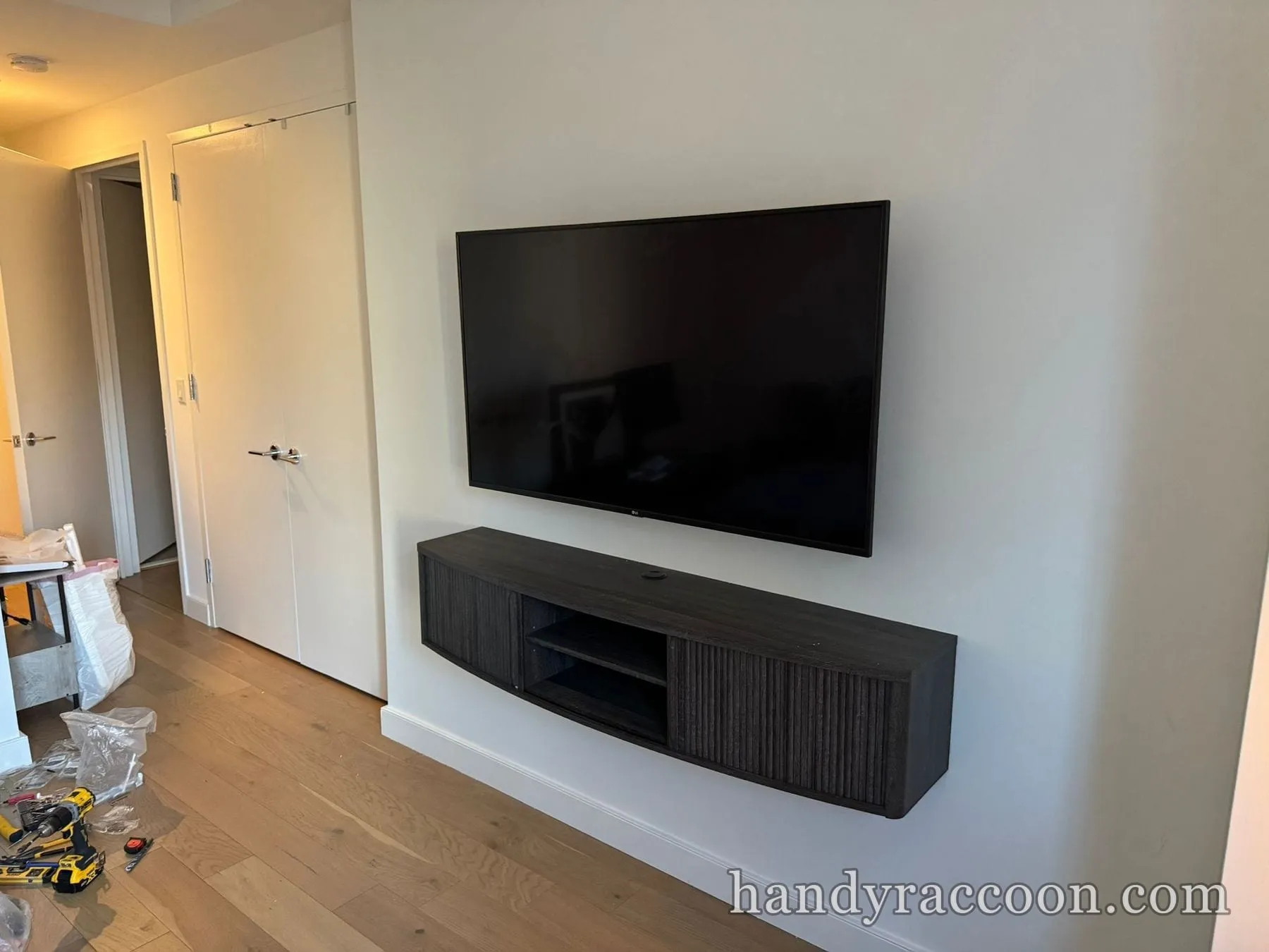 Black LG flat-screen TV mounted on a white wall above a dark wood floating media console.