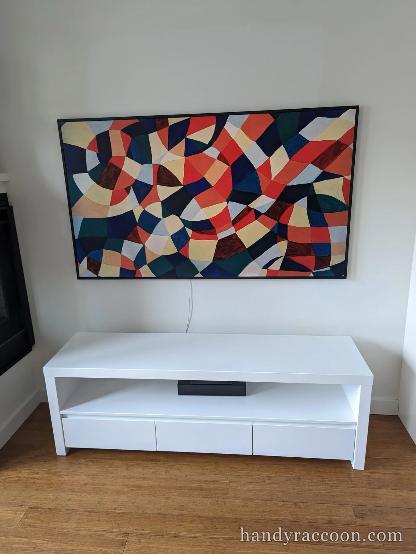 TV showing a colorful geometric abstract painting, mounted above a white media console.