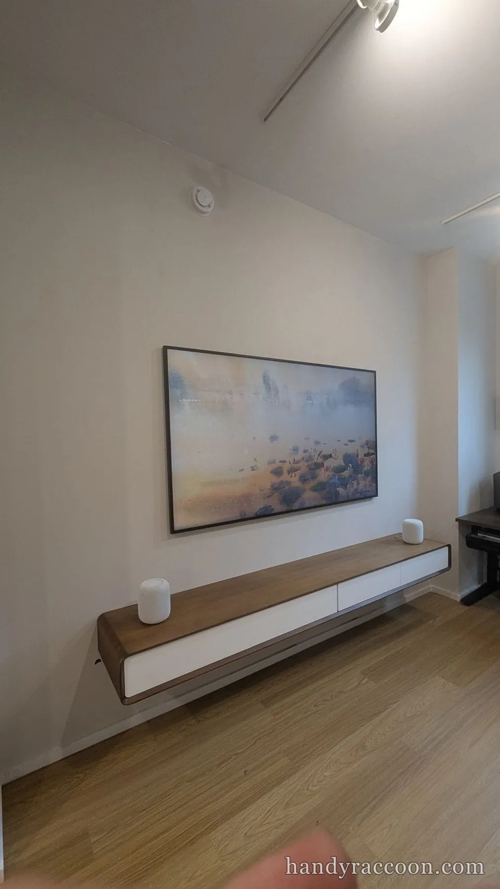 Flat-screen TV in art mode showing a landscape, above a floating console with two speakers.