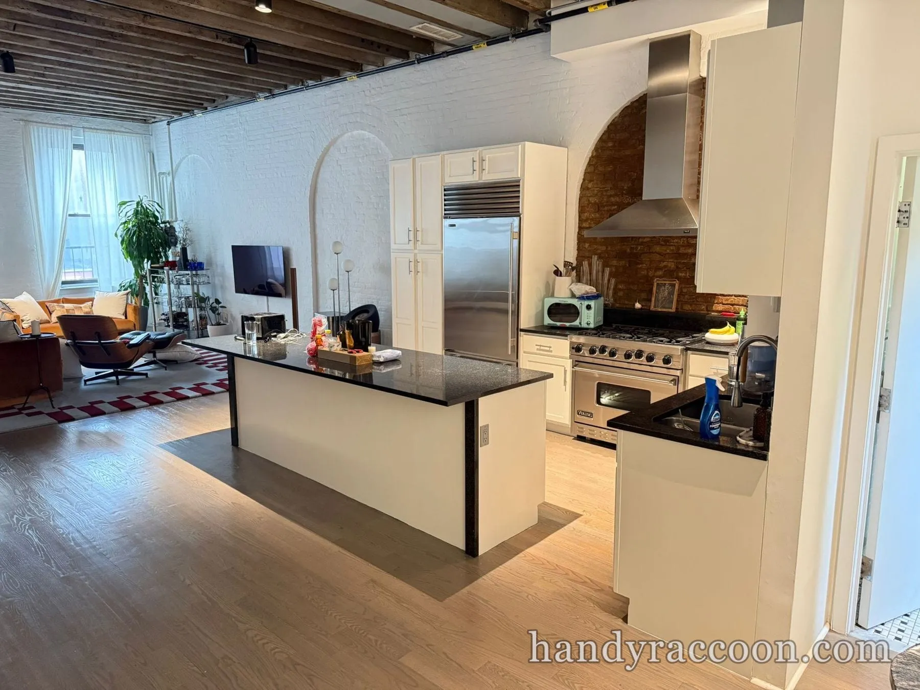 Wide loft view with white painted kitchen cabinets, a black granite island and a living area.
