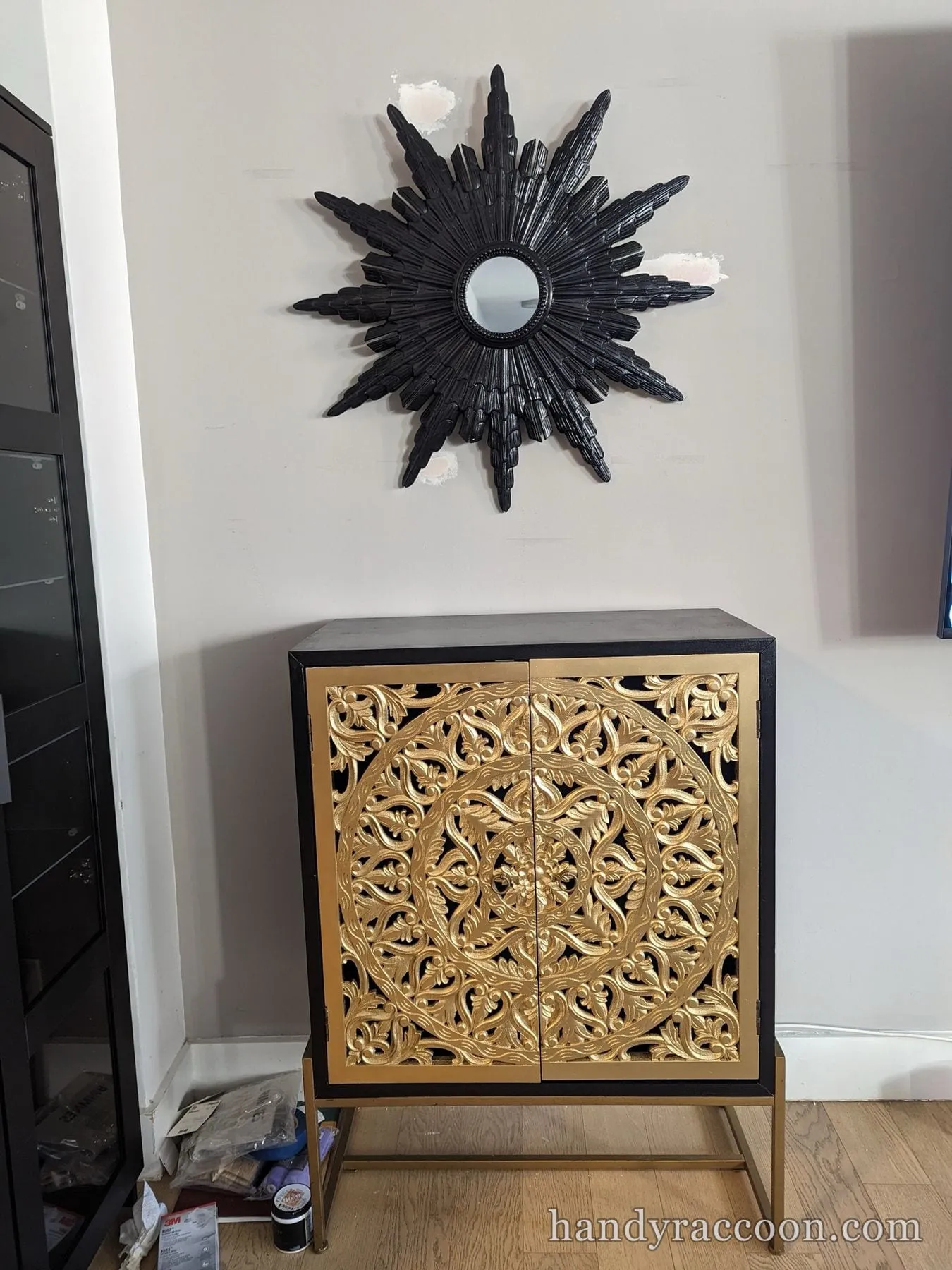 Sunburst wall mirror painted black with white brushed rays, lying on cardboard on the floor.