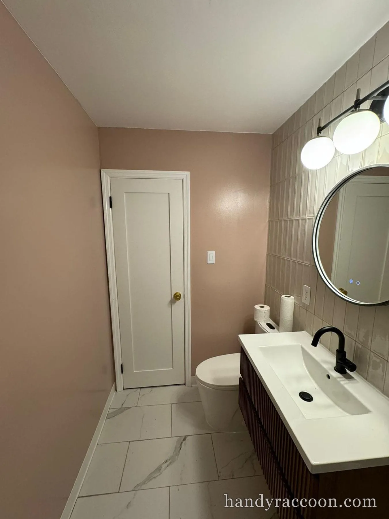 Finished bathroom with soft pink walls, white ceiling, tiled wall, floating vanity, and round mirror.