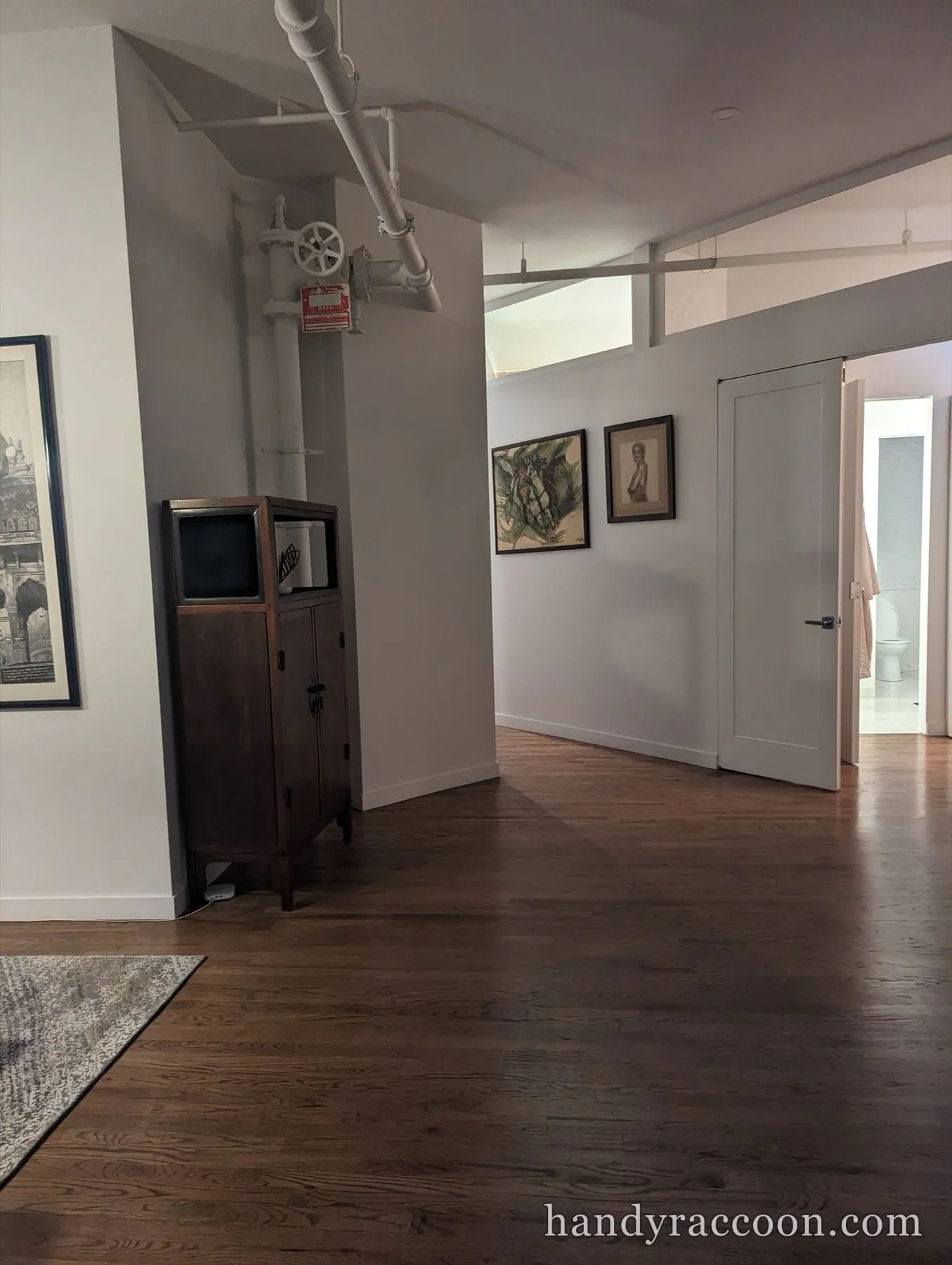 Loft hallway with white walls, framed art, a wood cabinet, and a white painted standpipe.
