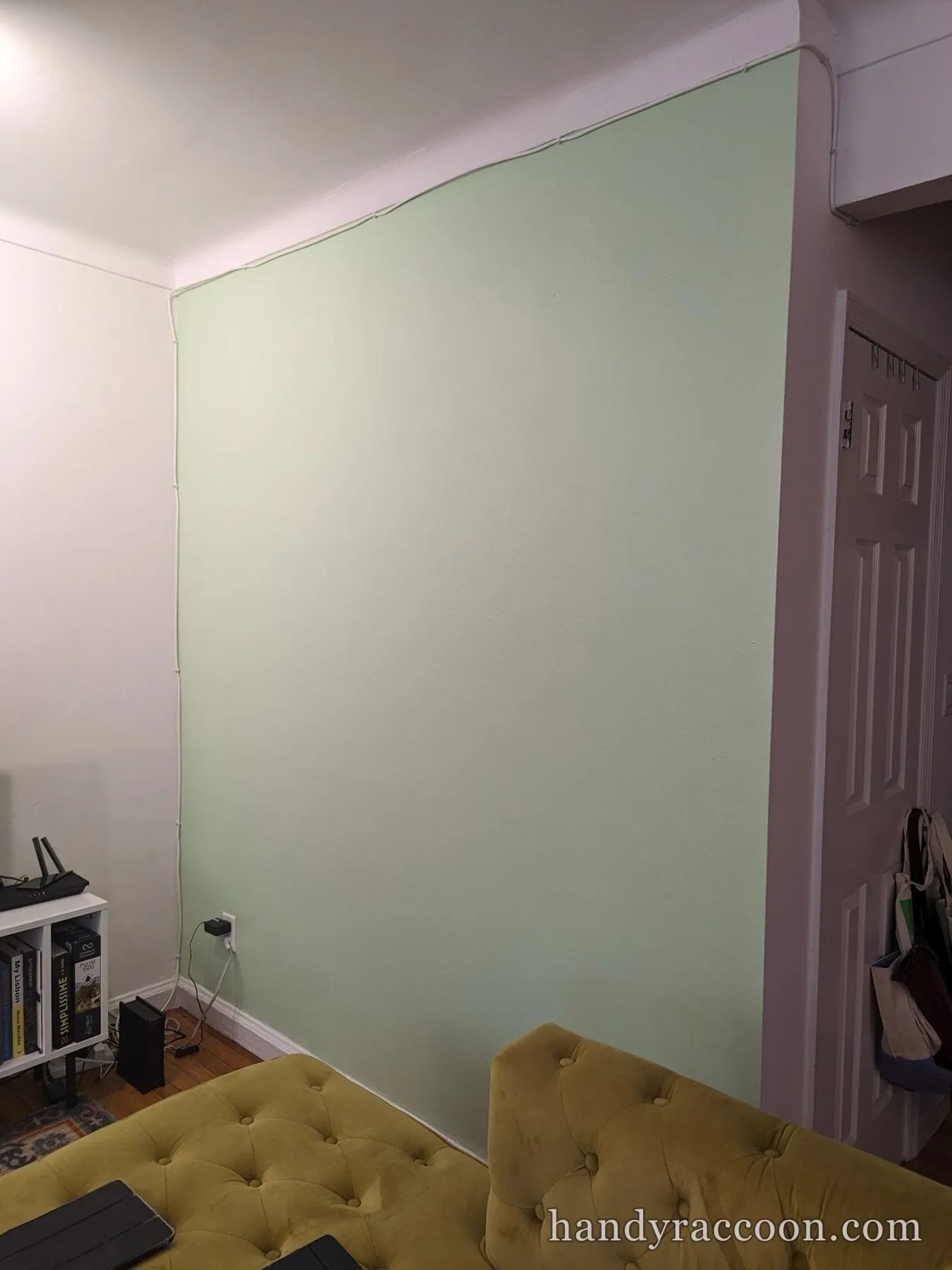 Living room with a large mint green accent wall, white side walls, and a mustard velvet sofa.