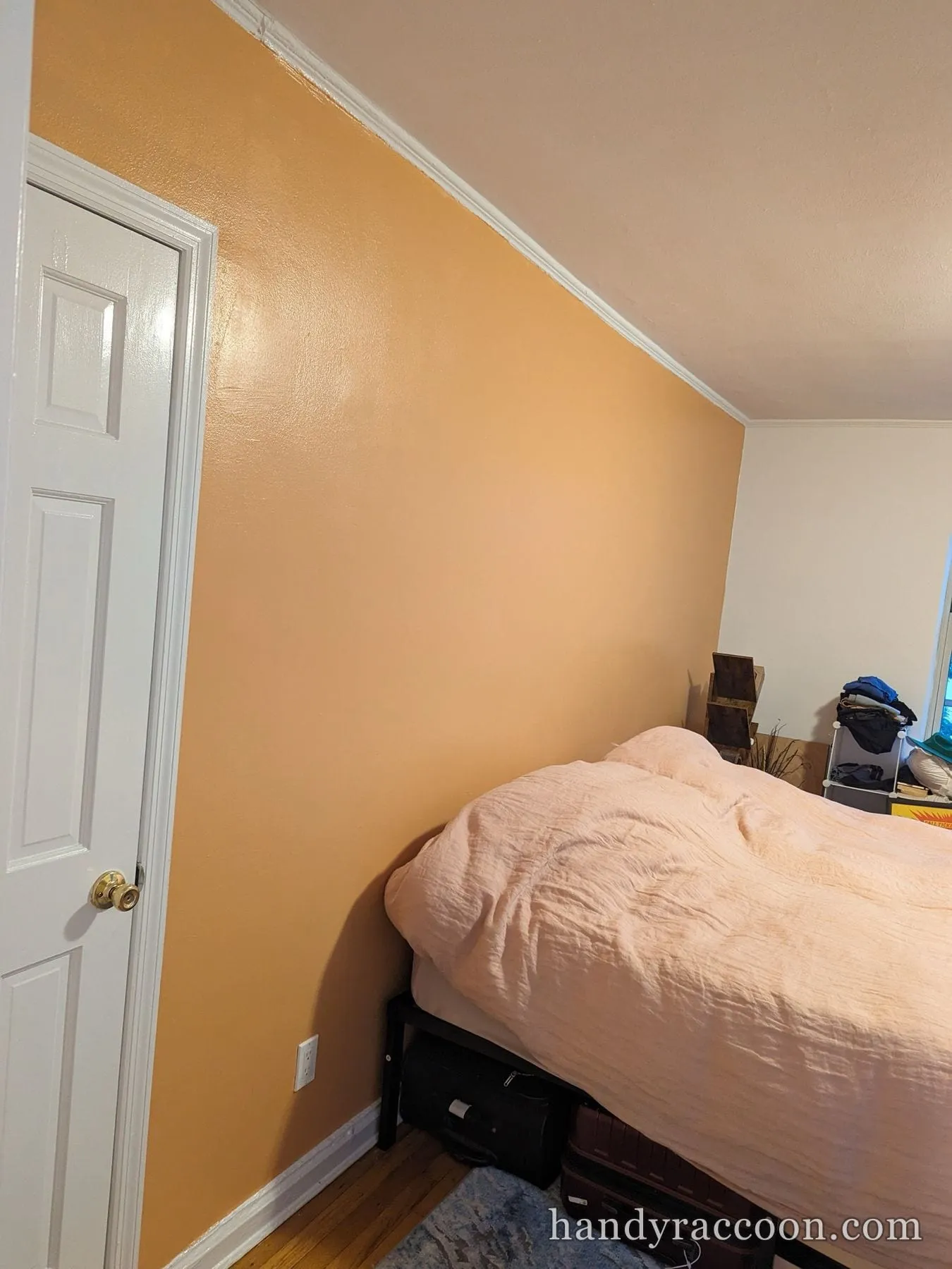 Bedroom accent wall painted warm orange, framed by white door and baseboard trim.