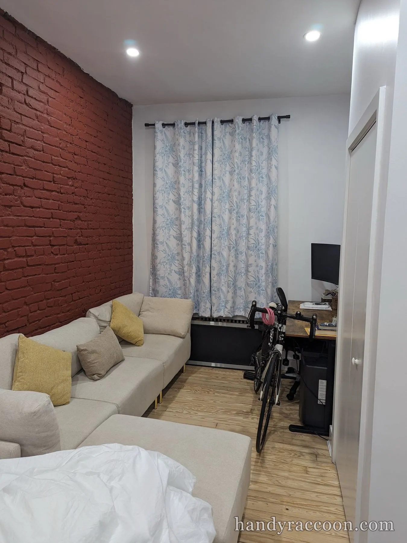 Small living room with white painted walls, red brick wall, sofa and curtained window.