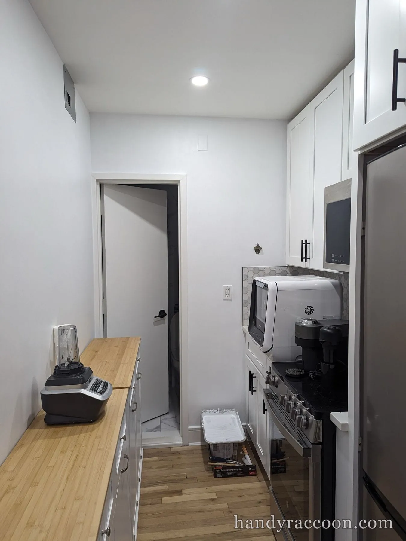 Narrow kitchen with freshly painted white walls, white cabinets and wood countertop.