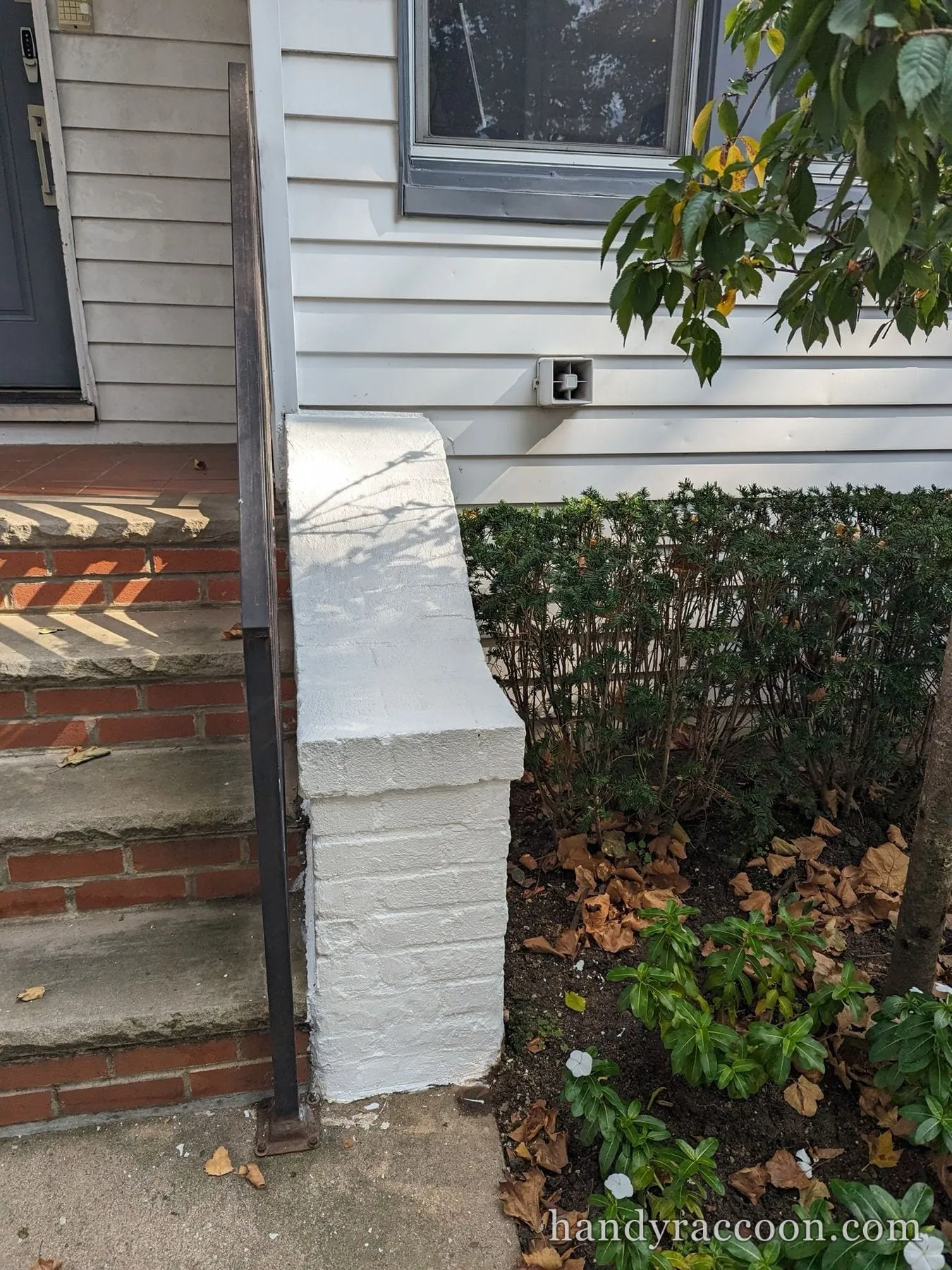 Freshly white painted masonry pier next to red brick front steps and a black handrail.