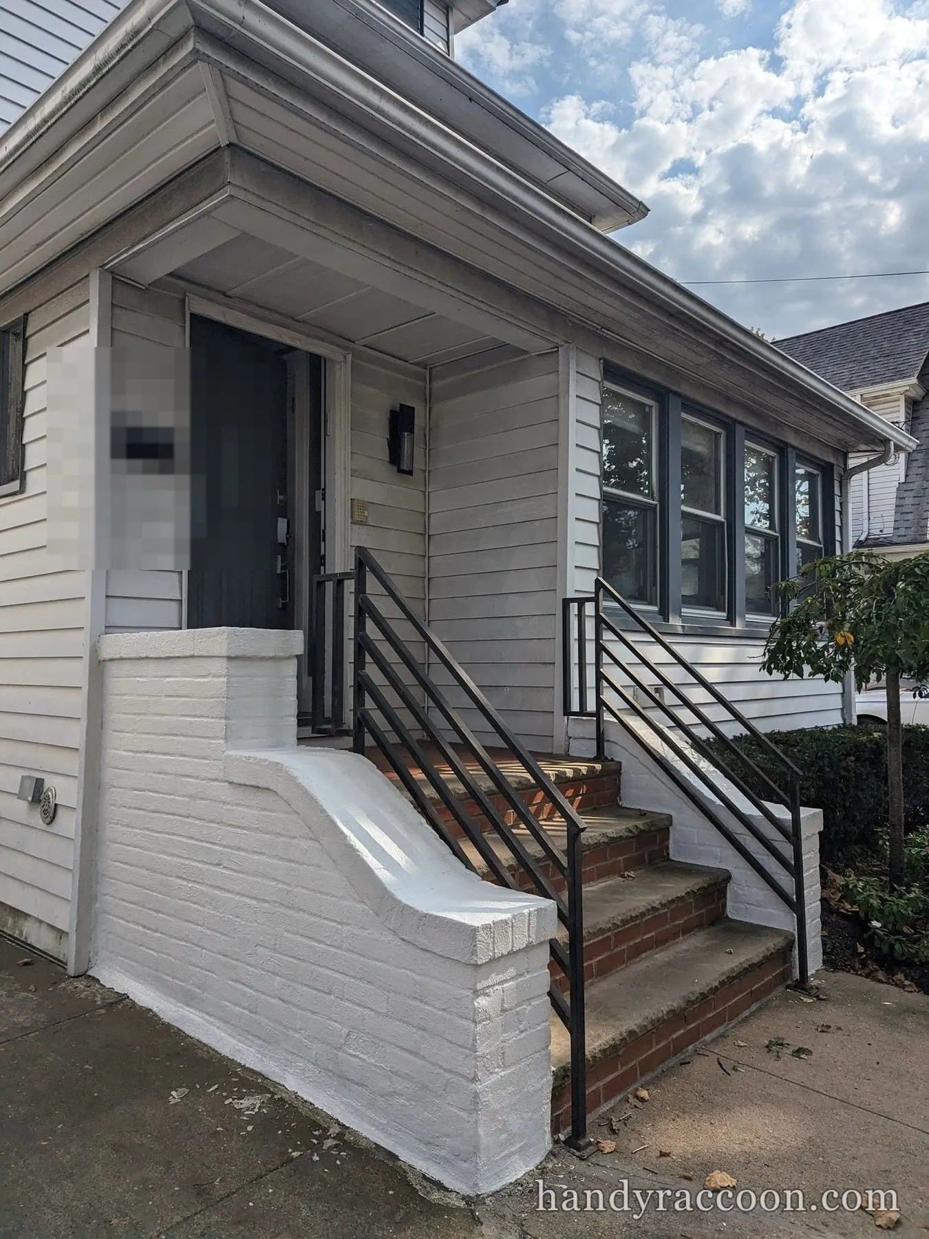 House exterior with white painted brick stoop walls and black railings on brick steps.