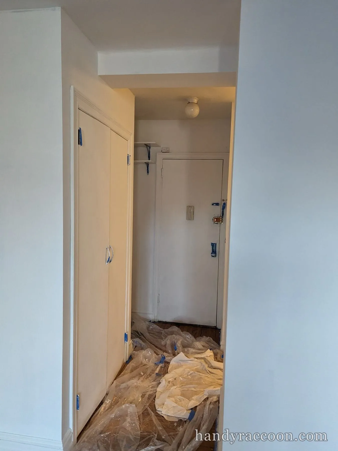 Apartment entry hall with white walls, plastic floor covering and taped door hardware.