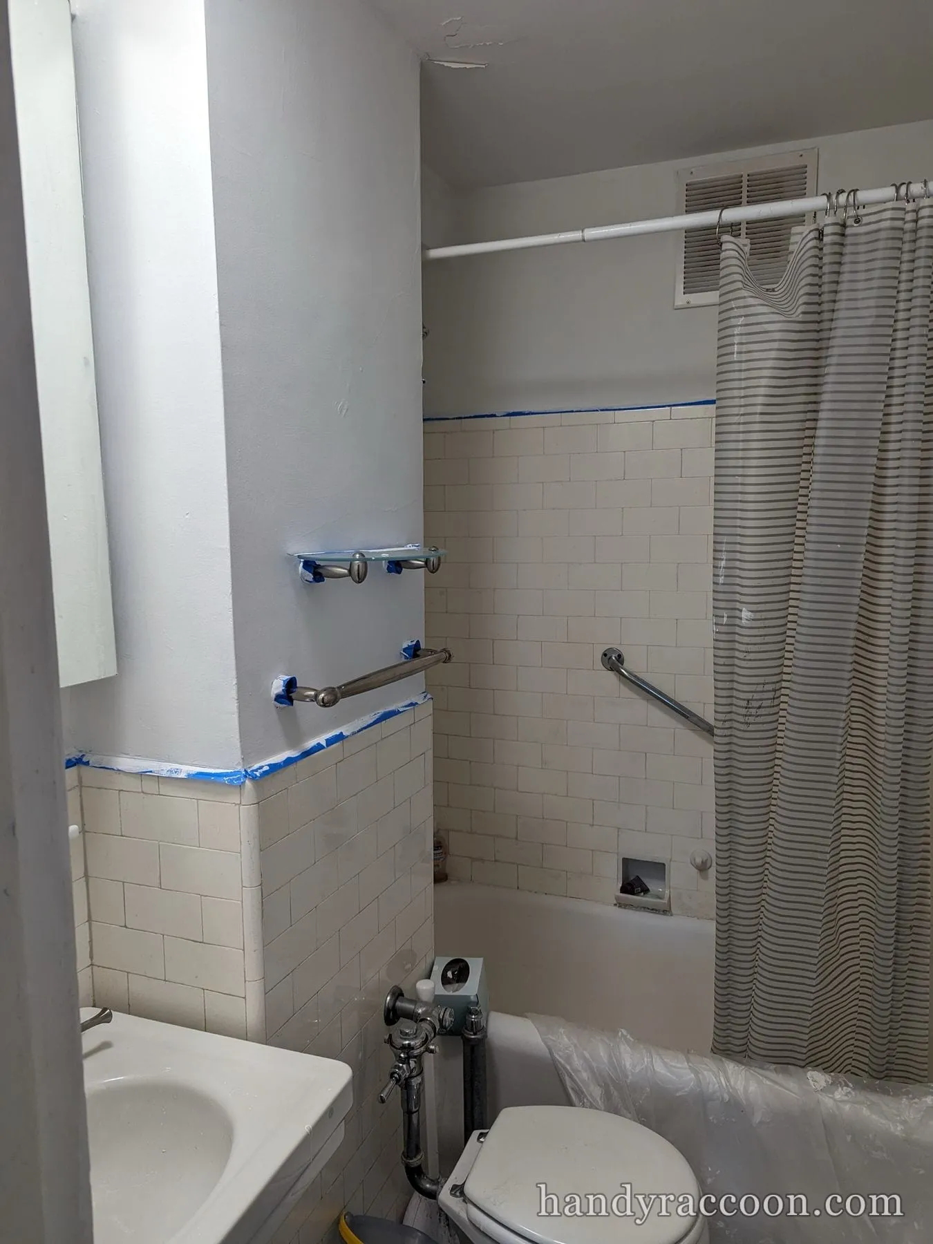 Bathroom mid painting with painter's tape along the tile line and taped towel bars.