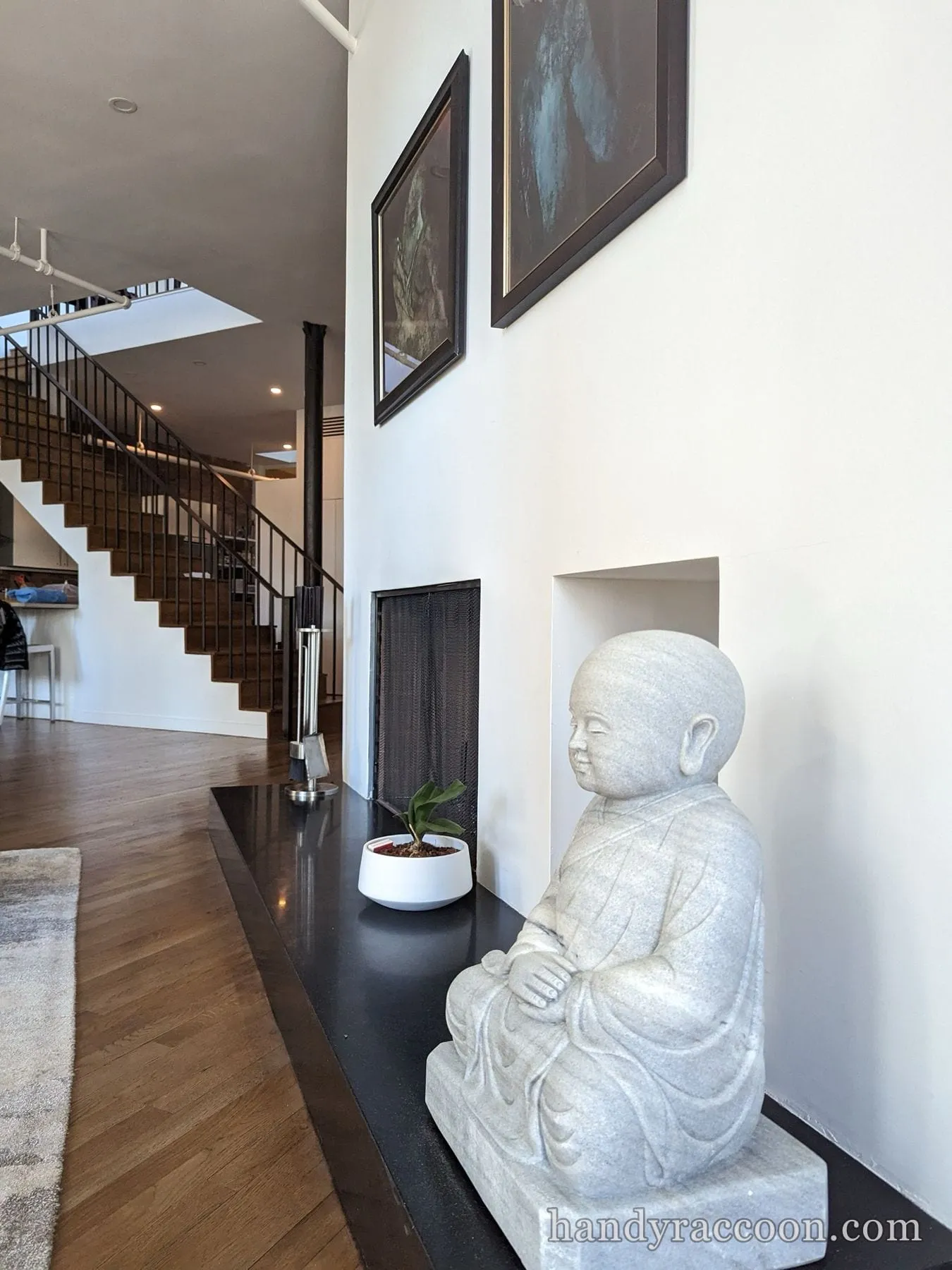 Loft interior with tall white painted walls, staircase, framed art and a stone statue.
