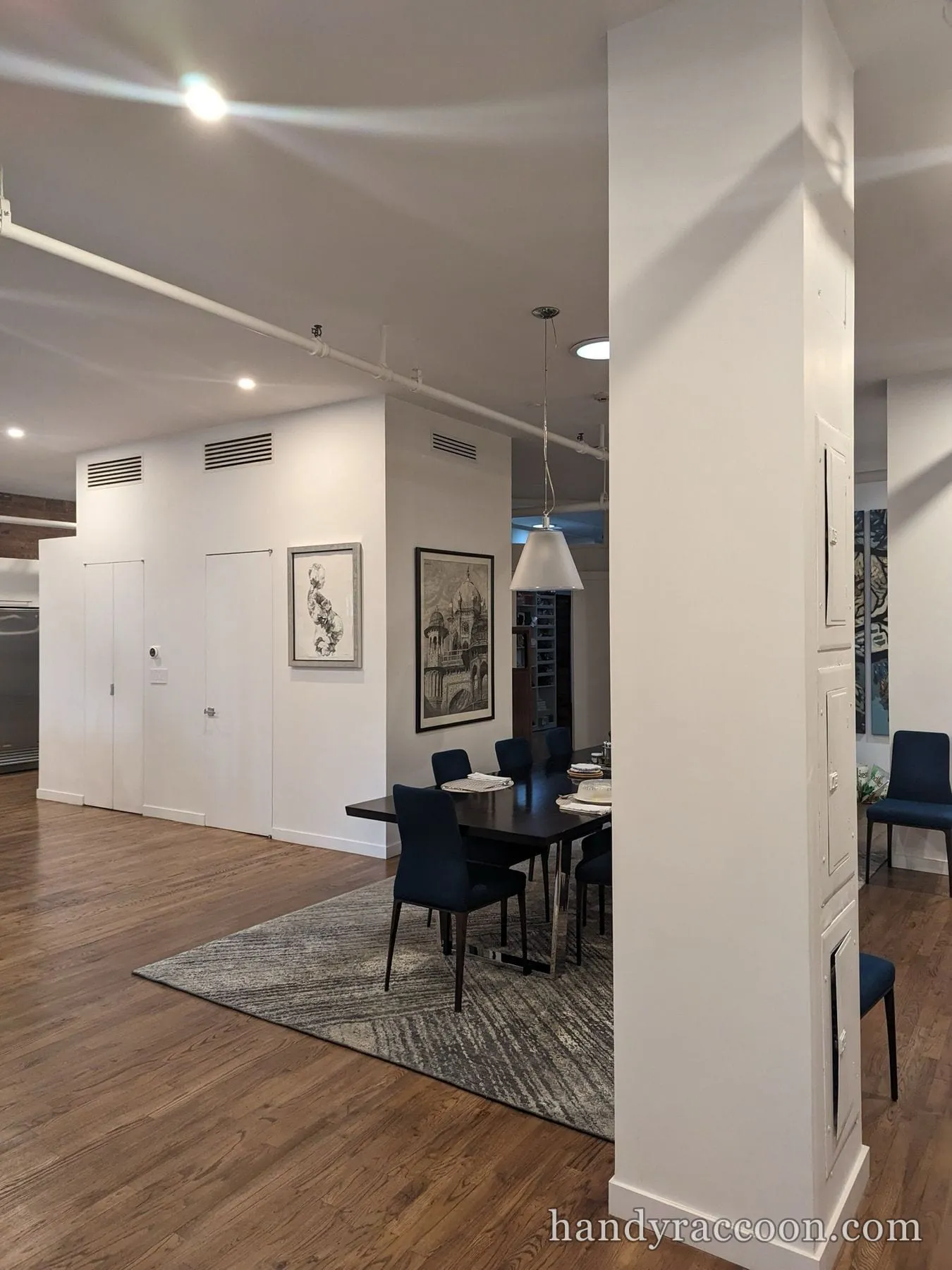 Dining table and blue chairs beside white painted loft walls and a square column.