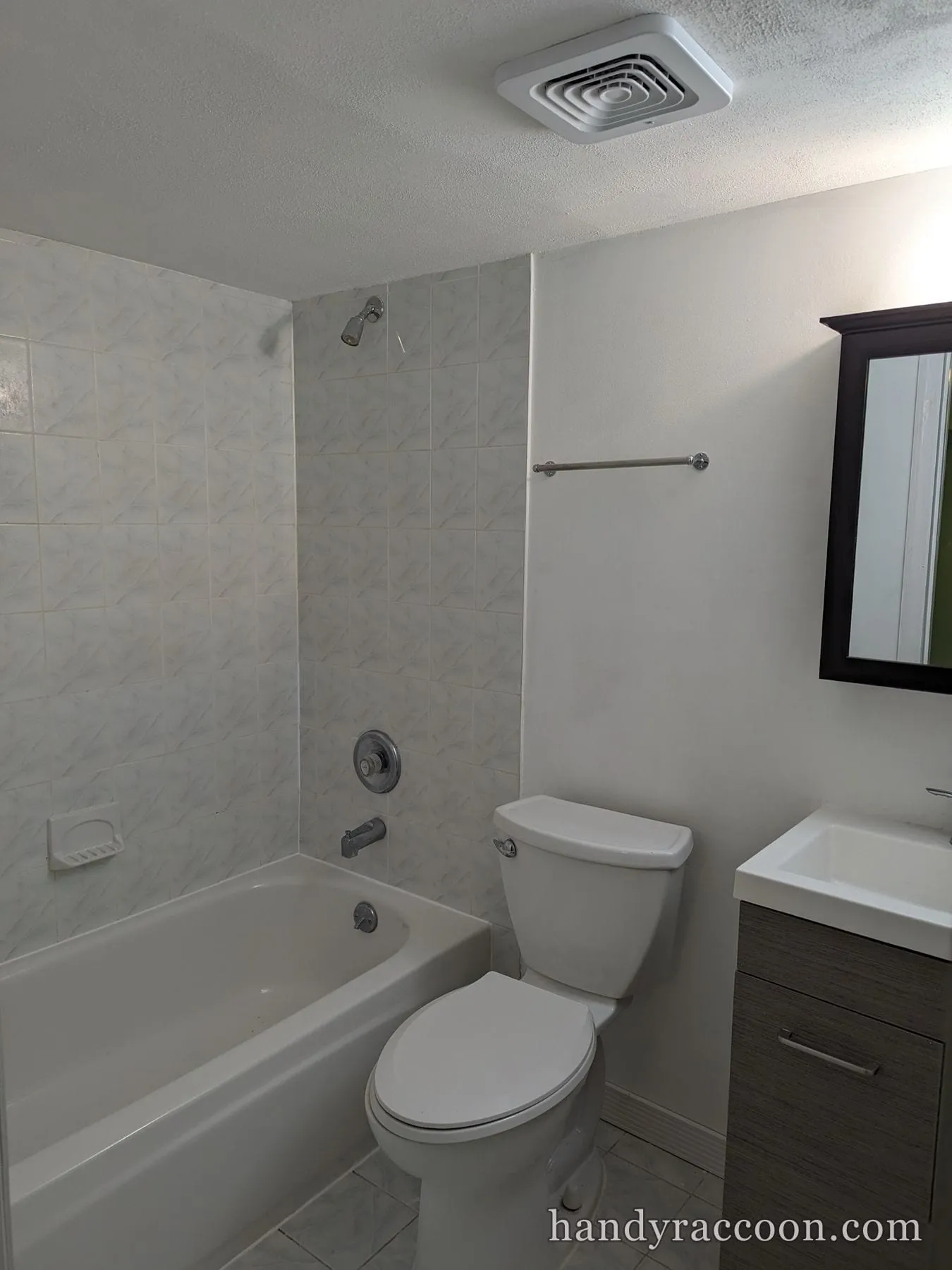 Bathroom with freshly painted white walls, tiled tub surround, toilet and wood vanity.