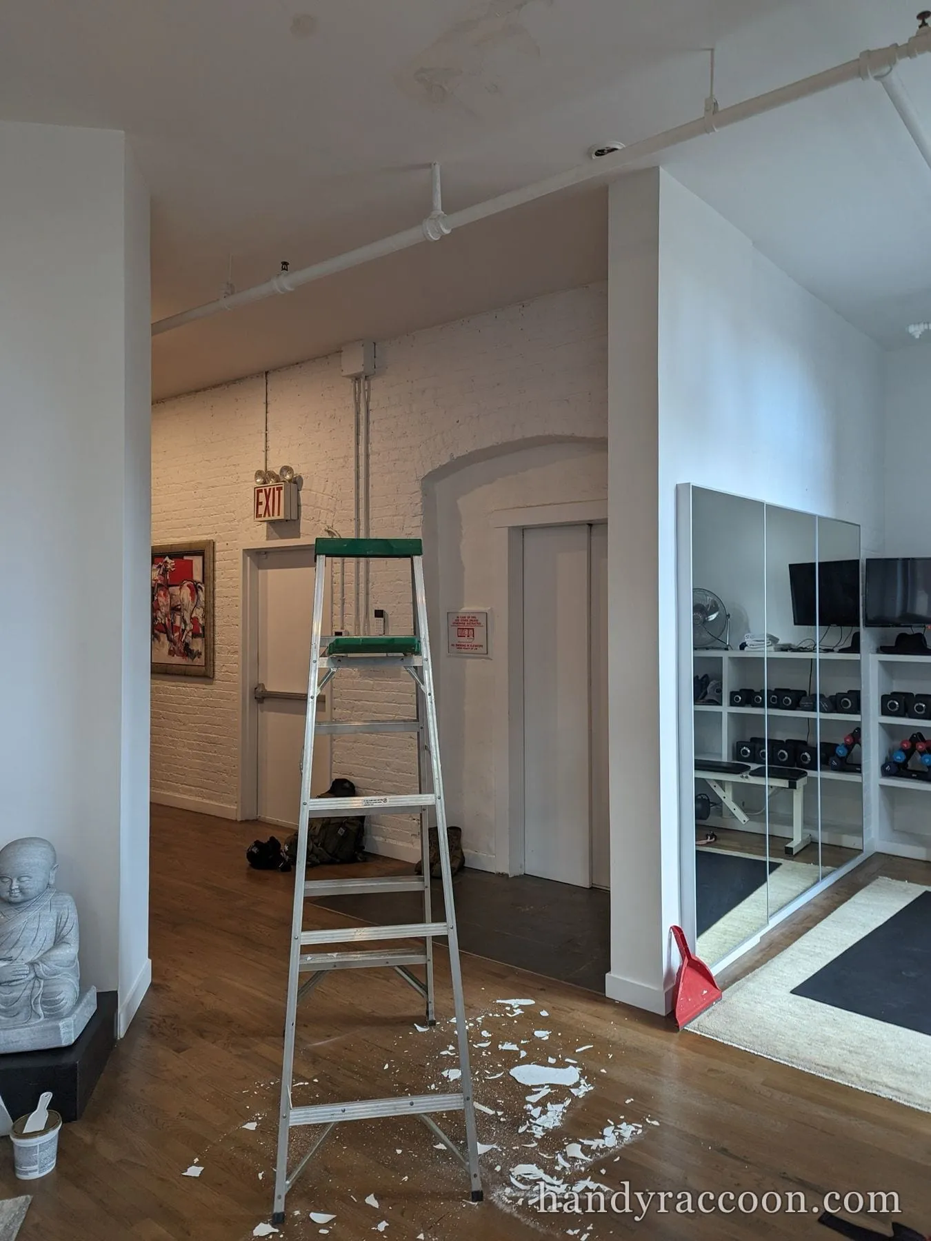 Loft corner with white painted brick, exit sign, elevator and a mirrored gym area.