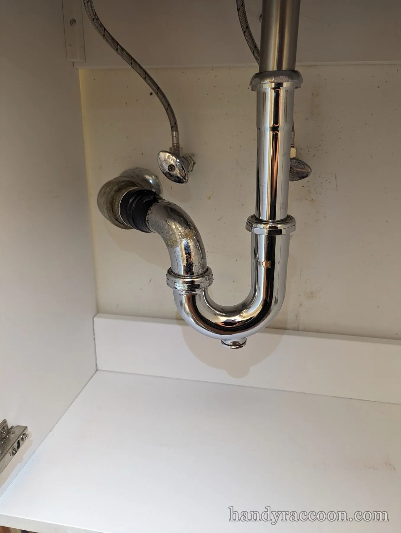 Newly installed shiny chrome P-trap and tailpiece under a white bathroom vanity cabinet.