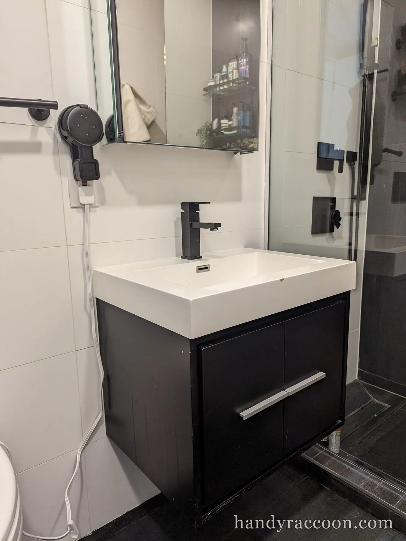 Wall-mounted black vanity with a white rectangular sink, black faucet, and mirror in a tiled bath.